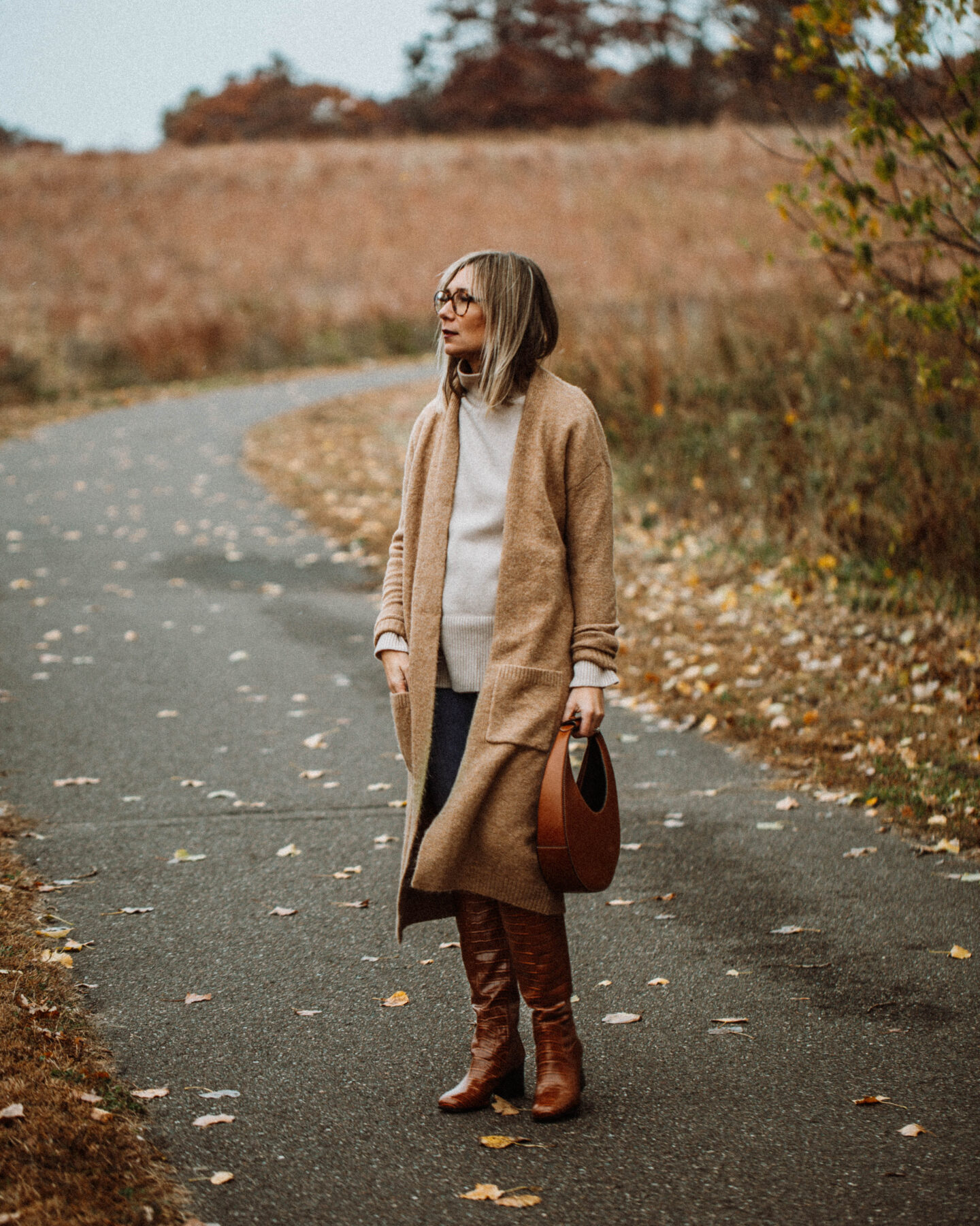 3 Cozy Outfits for Thanksgiving, camel duster maxi cardigan, taupe turtleneck sweater, blue skinny jeans, brownknee high croc effect boots, staud moon bag