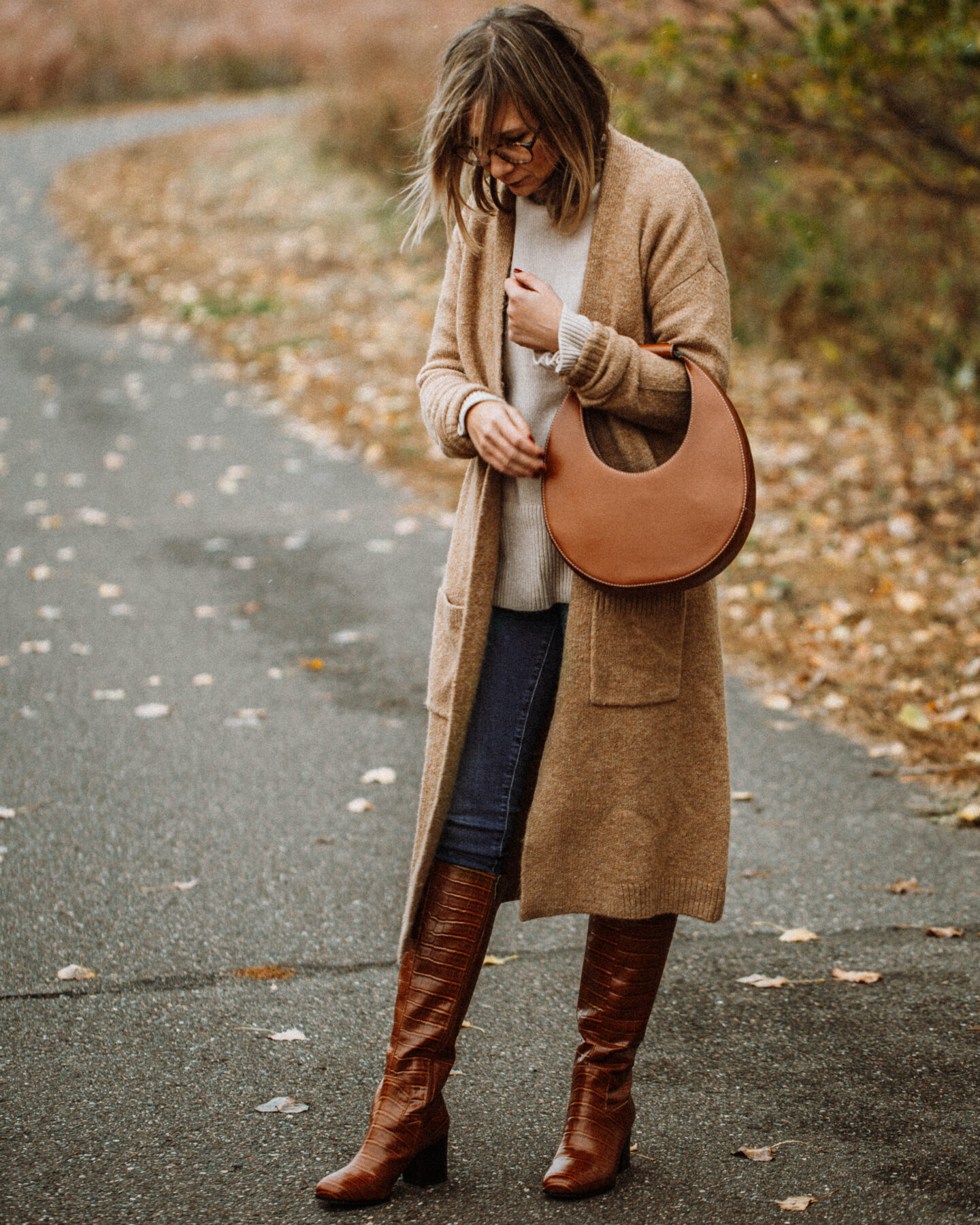 3 Cozy Outfits for Thanksgiving, camel duster maxi cardigan, taupe turtleneck sweater, blue skinny jeans, brownknee high croc effect boots, staud moon bag