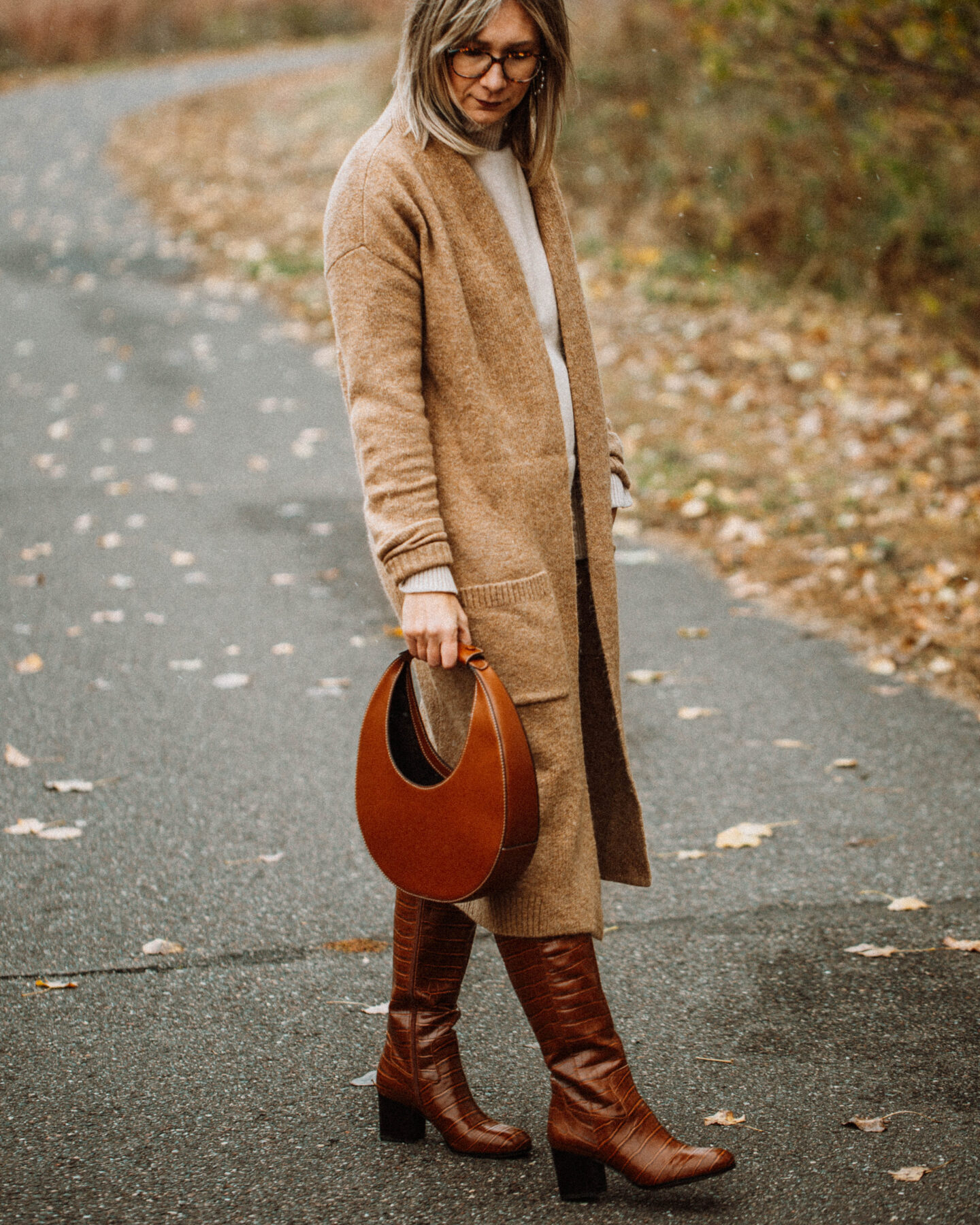 3 Cozy Outfits for Thanksgiving, camel duster maxi cardigan, taupe turtleneck sweater, blue skinny jeans, brownknee high croc effect boots, staud moon bag