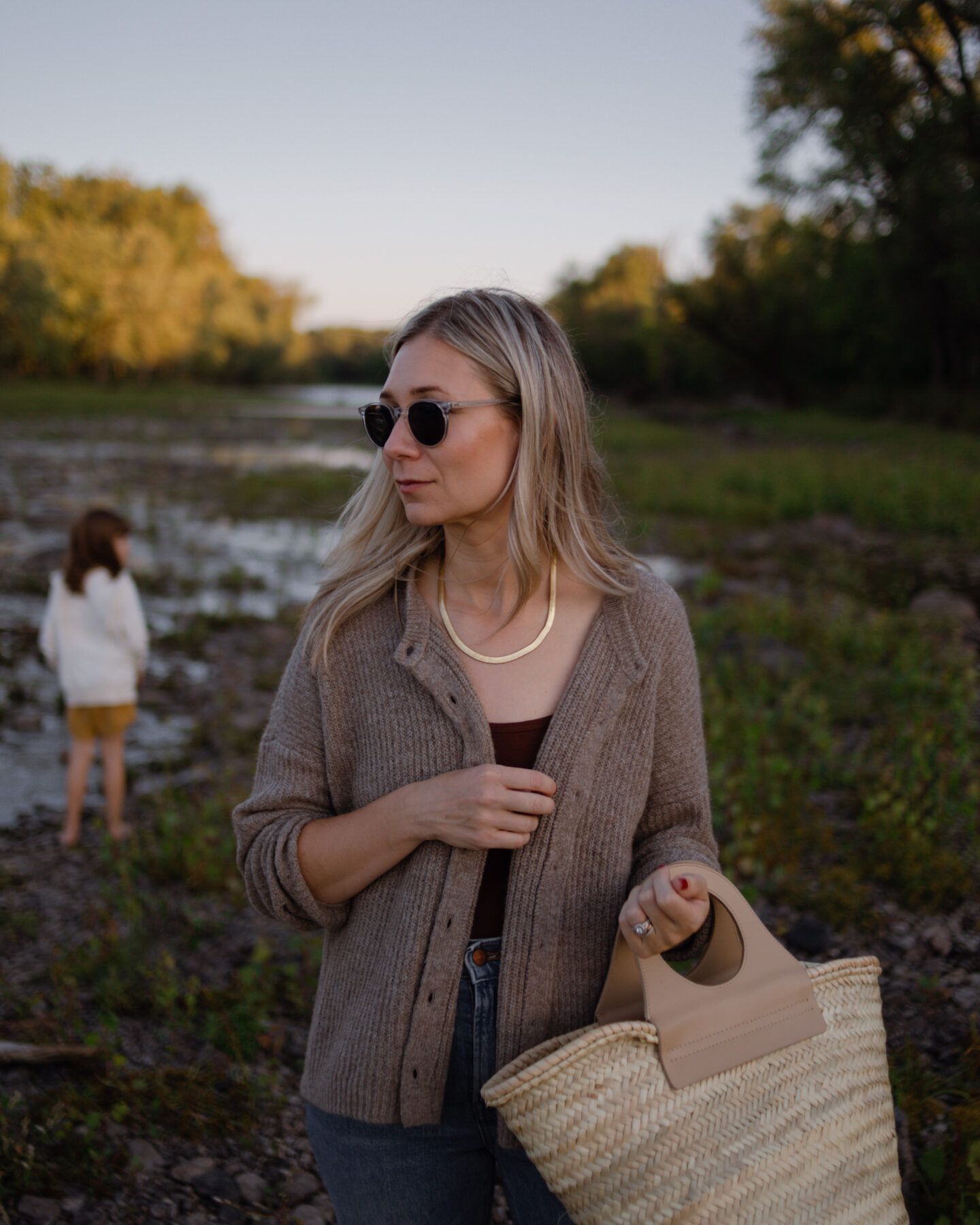 girl standing in front of a river wearing a cozy Madewell sweater and carrying a basket bag