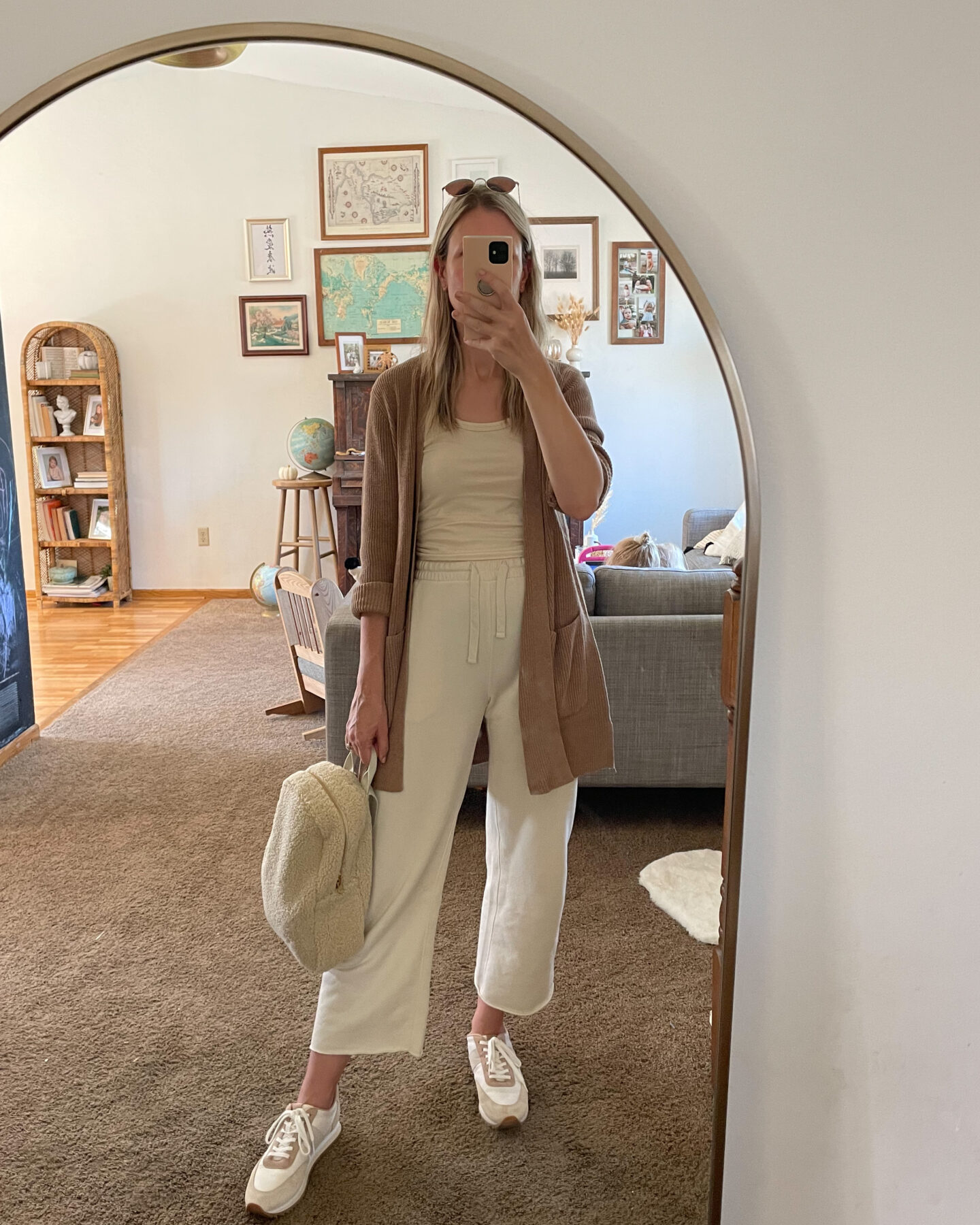 Karin Emily wears a cream loungewear set with a camel cardigan on top, a pair of sneakers and a sherpa bag