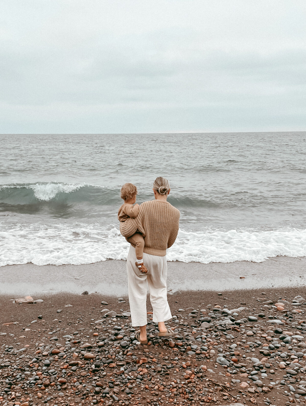 karin emily standing on the beach wearing the babaa jumper no 18 in clay pot and a pair of waffle knit mate the label wide leg louneg pants