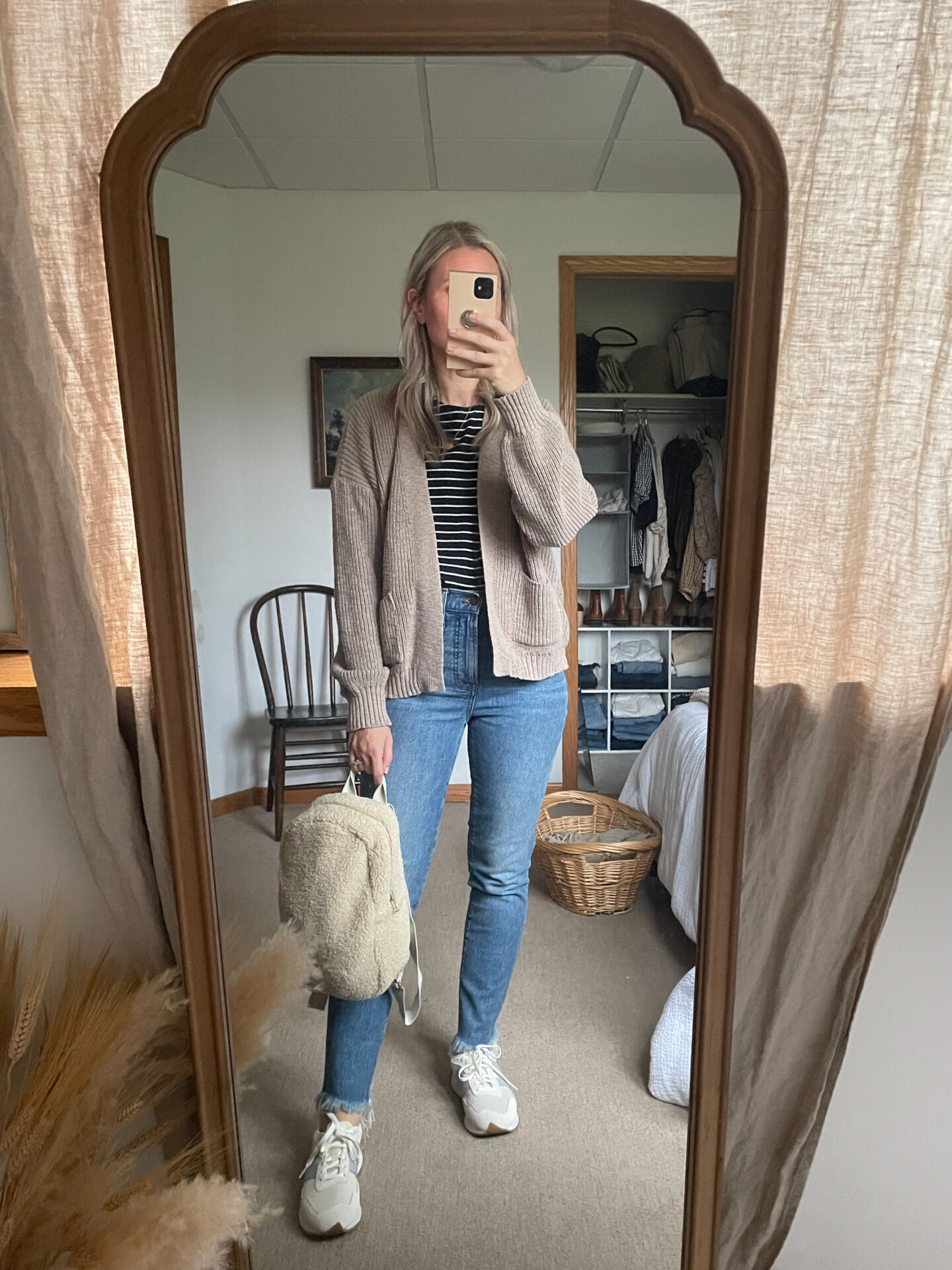 Karin Emily wears a sustainably made cardigan, striped tee, perfect vintage jeans from madewell, new balance sneakers, and a sherpa bag