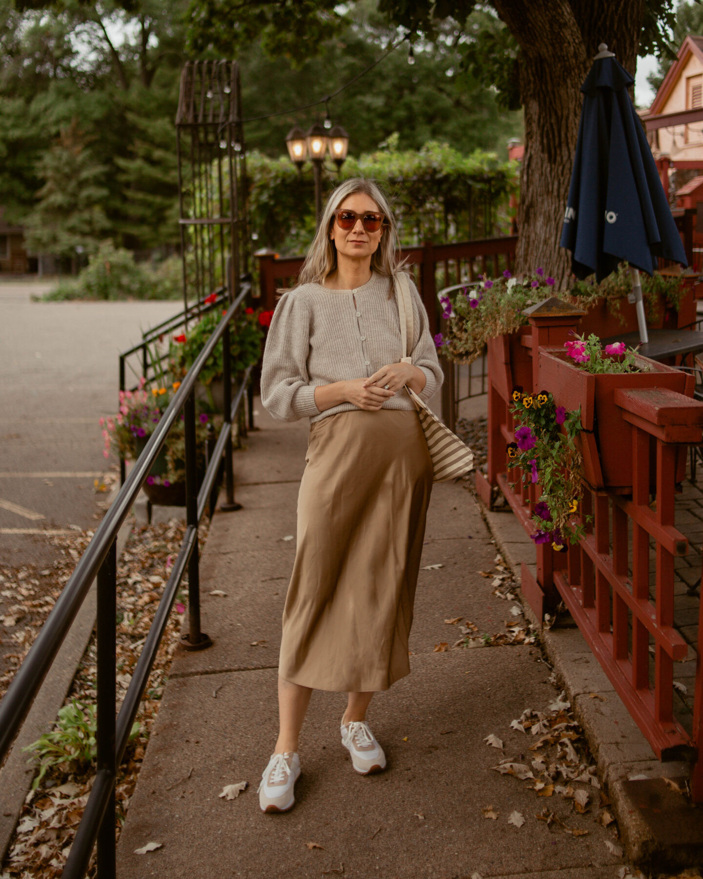 Karin Emily wears a comfy and chic fall outfit: a puff sleeve cardigan with a camel colored slip skirt and a pair of tennis shoes