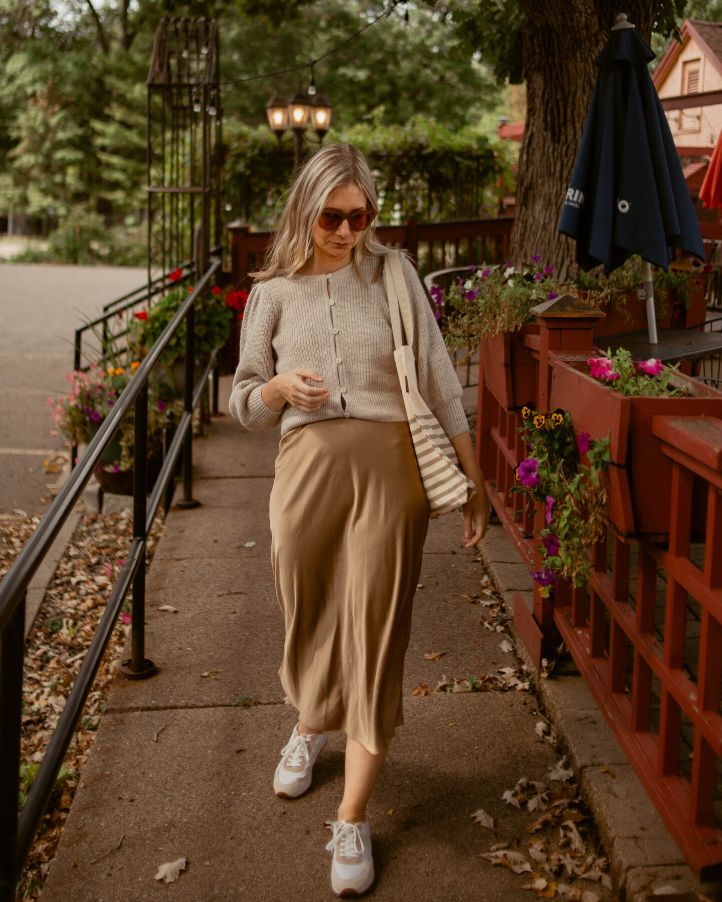Karin Emily wears a puff sleeve cardigan with a camel colored slip skirt and a pair of tennis shoes