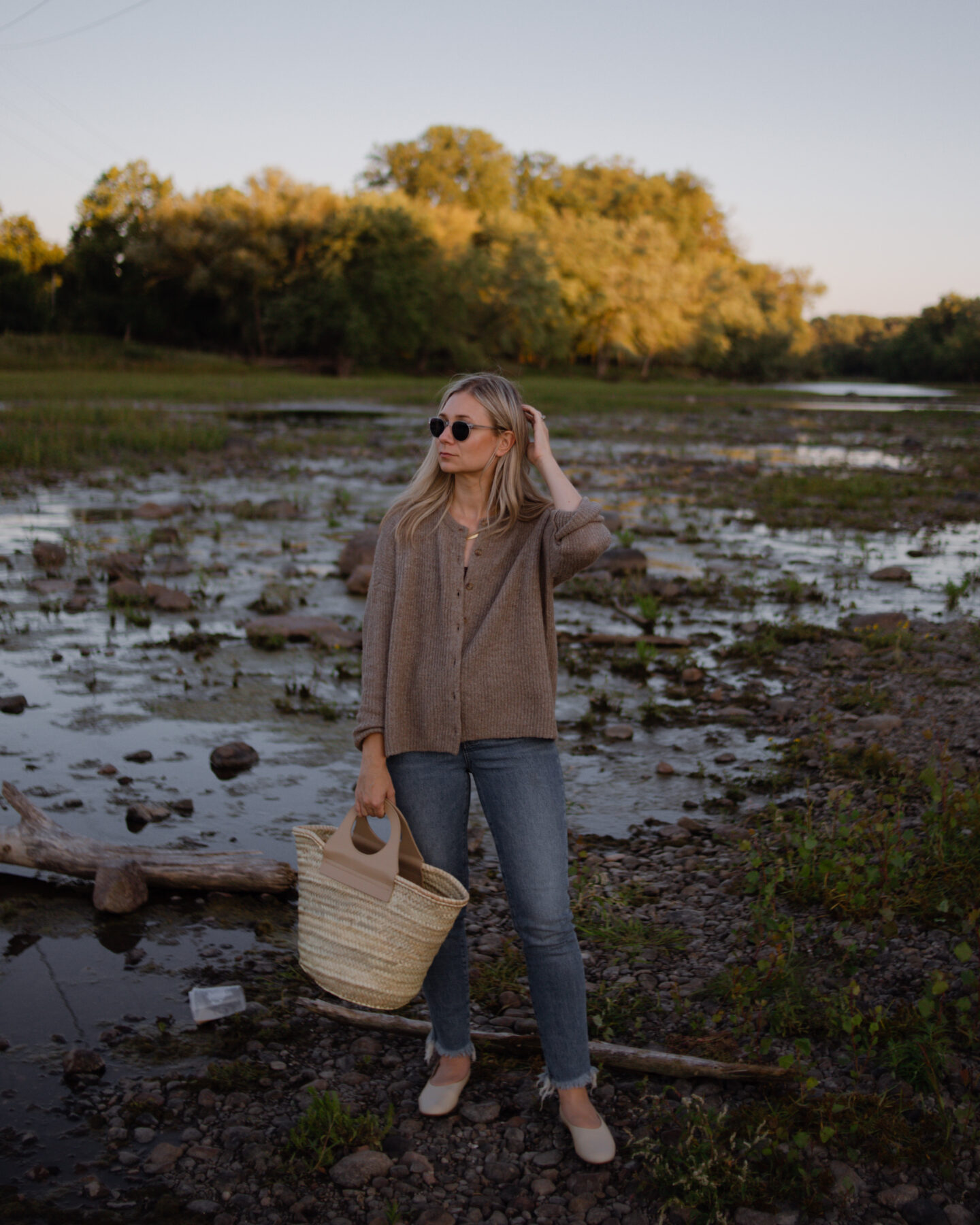 girl standing in front of a river wearing a cozy Madewell sweater and perfect vintage jeans from Madewell carrying a Hereu basket bag