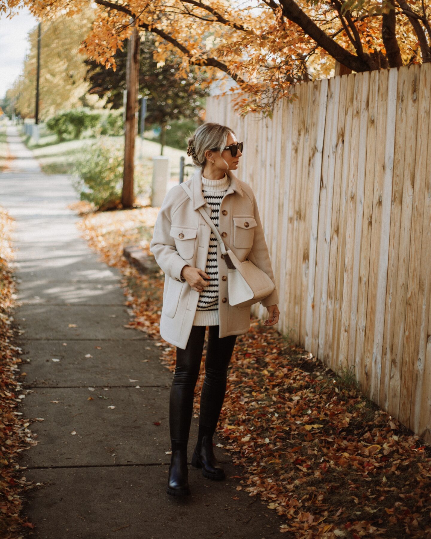 Karin Emily wears a striped sweater tunic under a neutral shacket and leather leggings with black lug boots