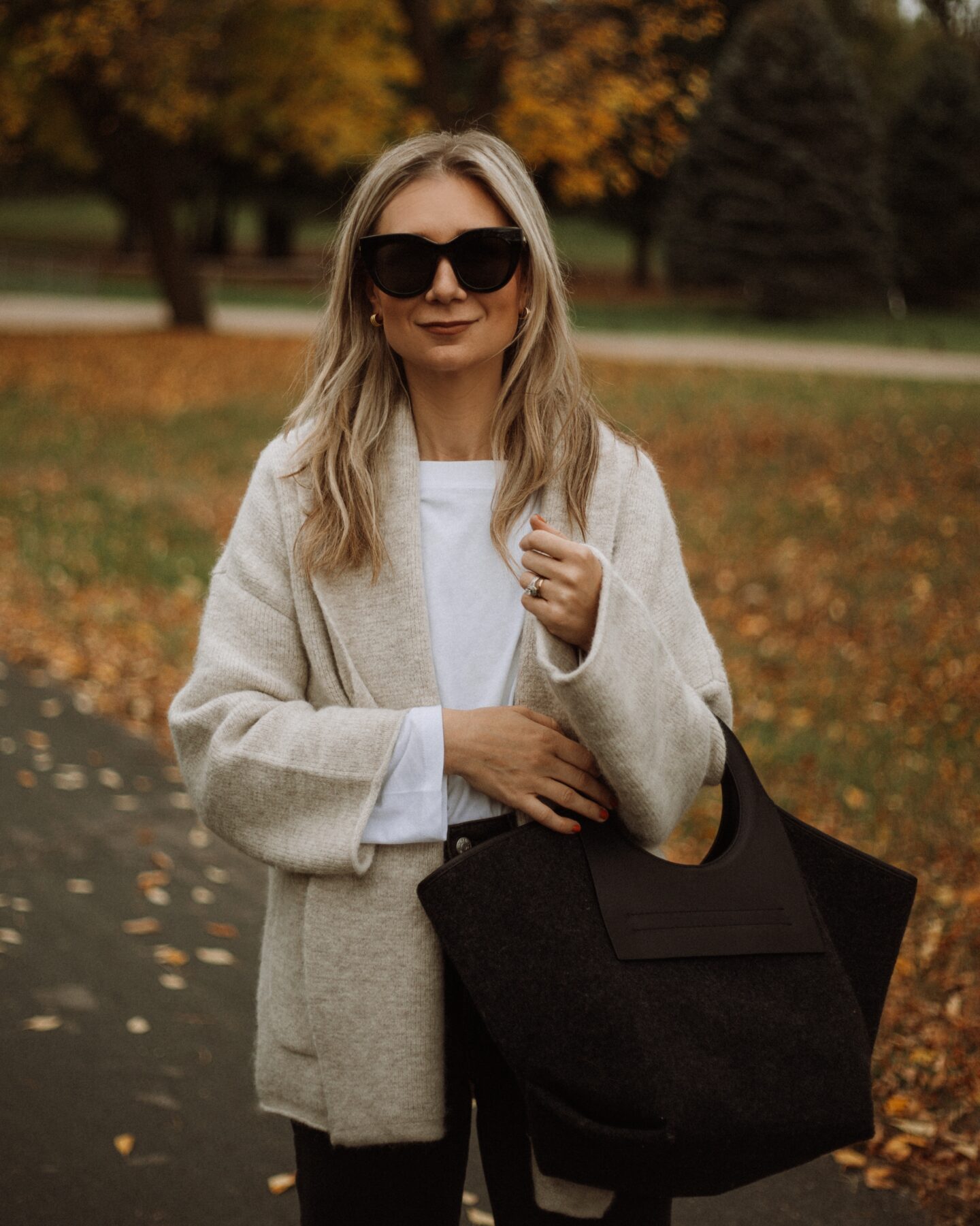 Karin Emily wears a Madewell shawl cardigan, white tee, black madewell perfect vintage jeans, and a wool Hereu bag,