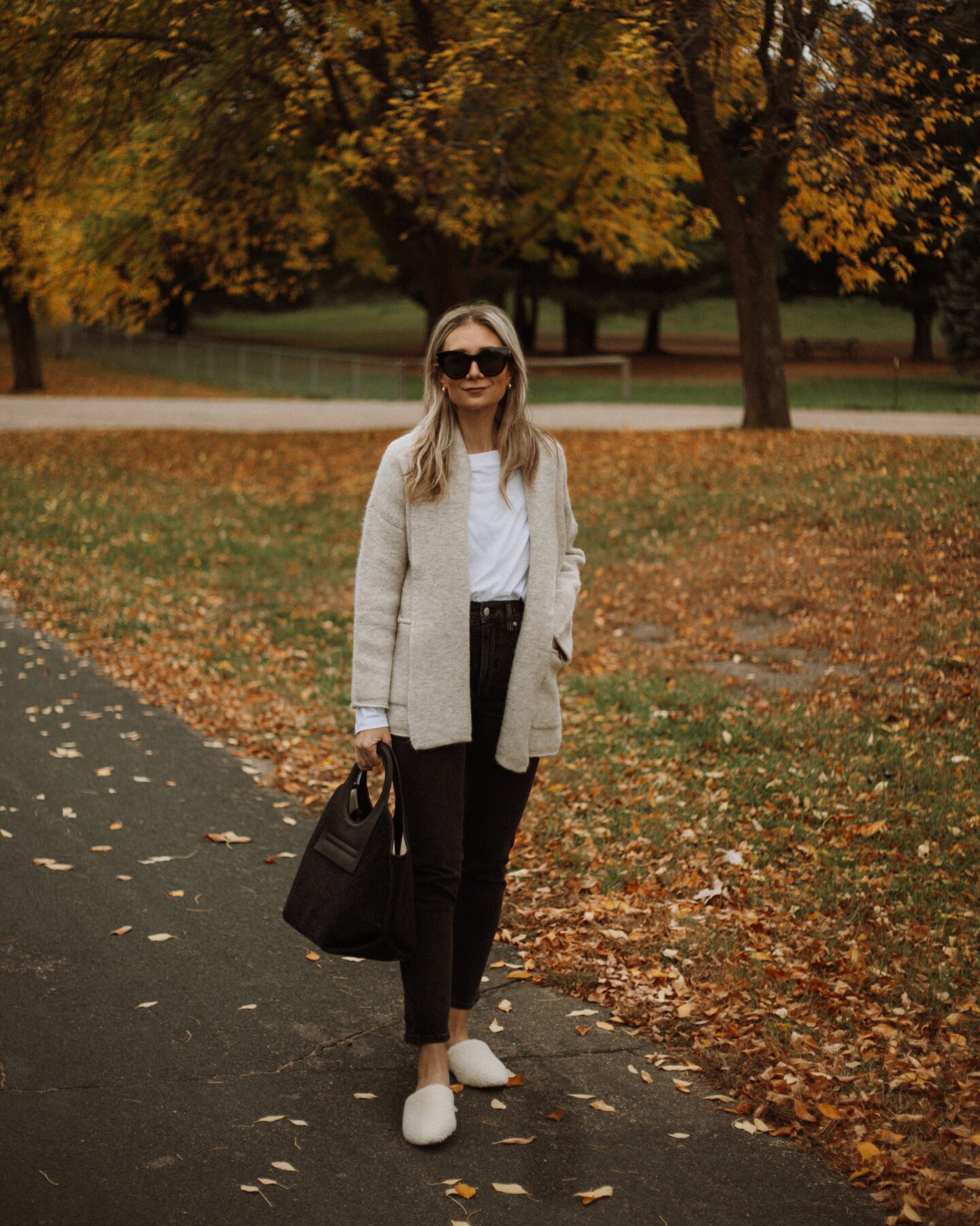 Karin Emily wears a Madewell shawl cardigan, white tee, black madewell perfect vintage jeans, a wool Hereu bag, and sherpa mules