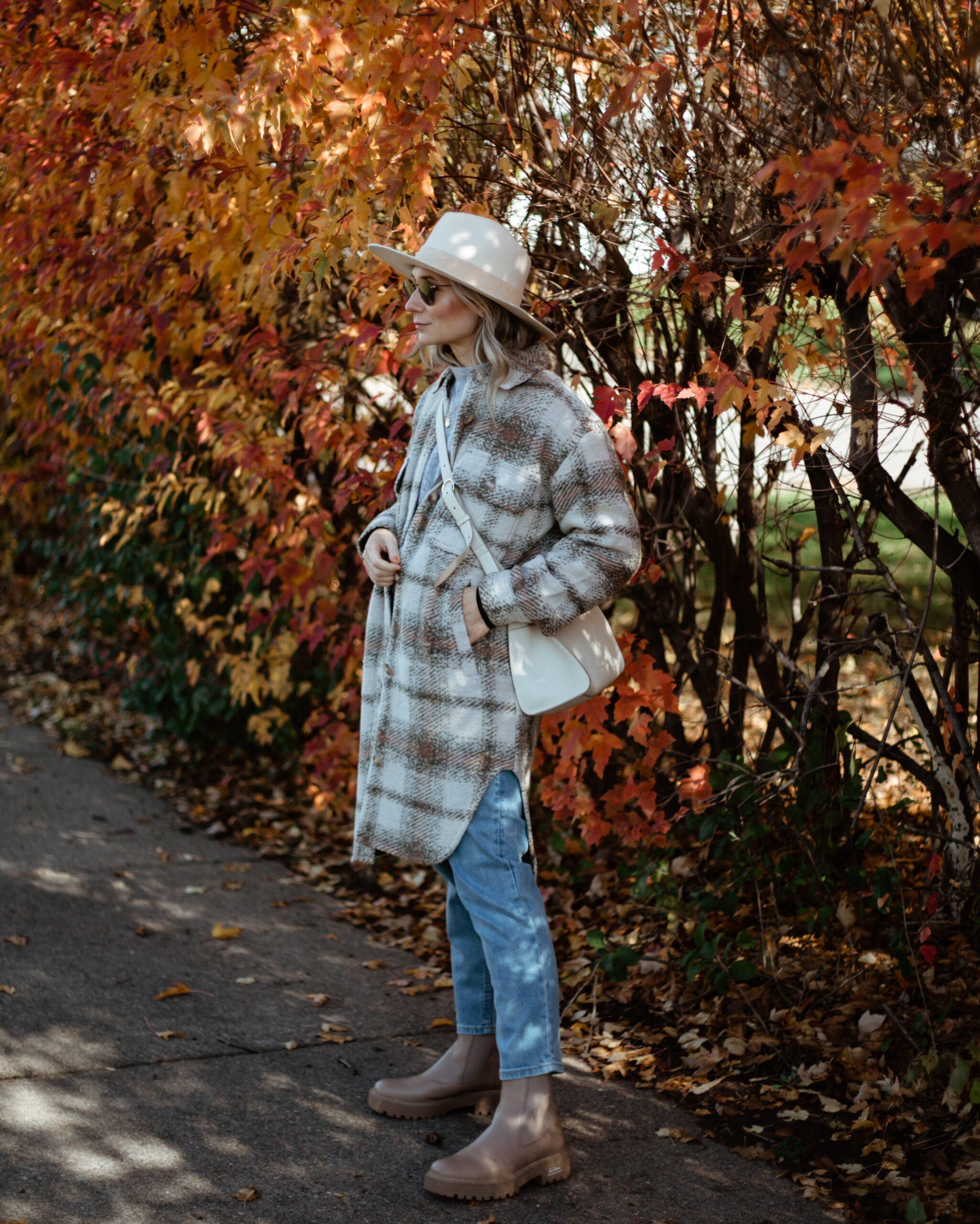 Karin Emily wears a plaid shacket, light wash jeans, a cream hat, and tan lug boots