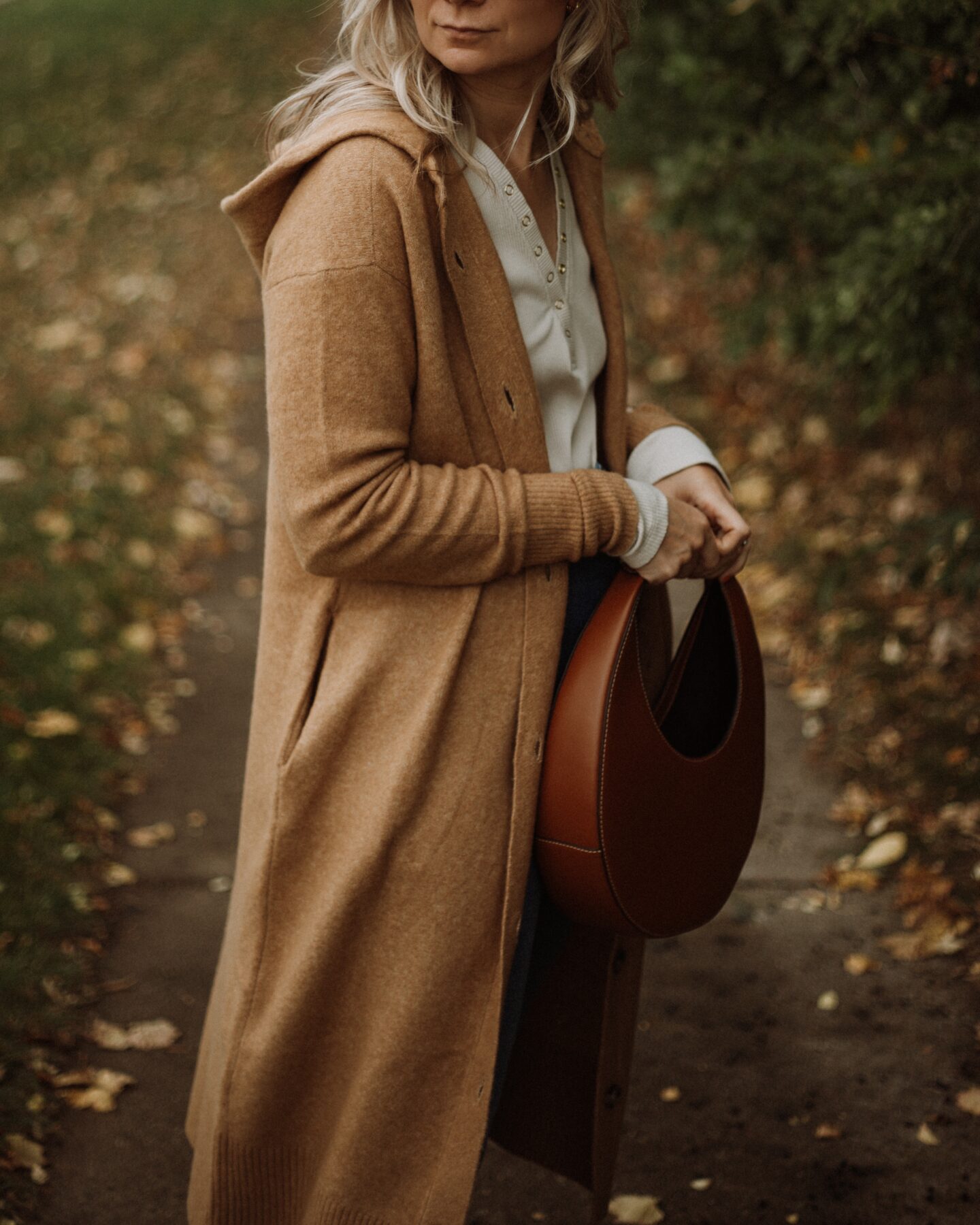 Karin Emily wears a long maxi cardigan from Everlane, a henley tee, and a staud moon bag