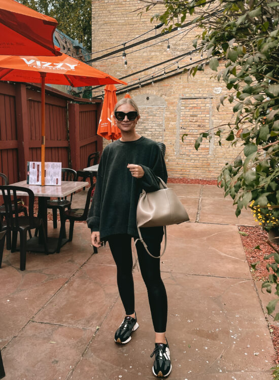 Karin Emily wears an oversized sweatshirt from free people over spanx faux leather leggings, and black and white new balance sneakers with a polene bag and black le specs air heart sunglasses