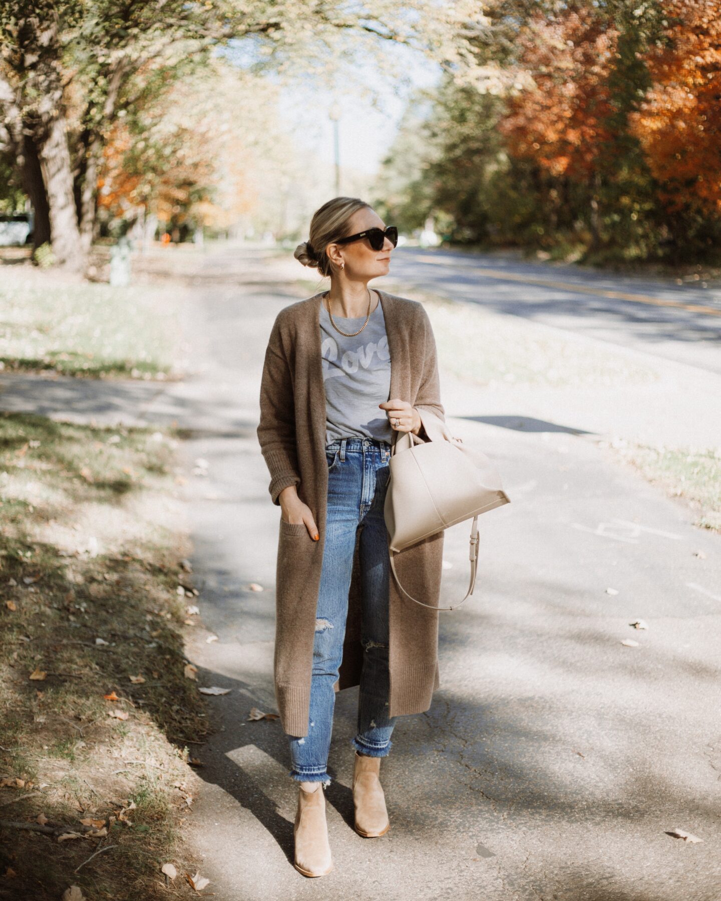 Karin Emily wears a graphic tee, cashmere cardigan, suede booties, and distressed jeans