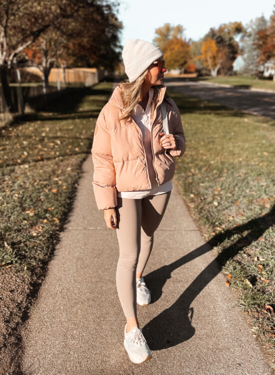 Karin Emily wears a fall sporty outfit with a pink track zip up, pink puffer coat, and taupe leggings