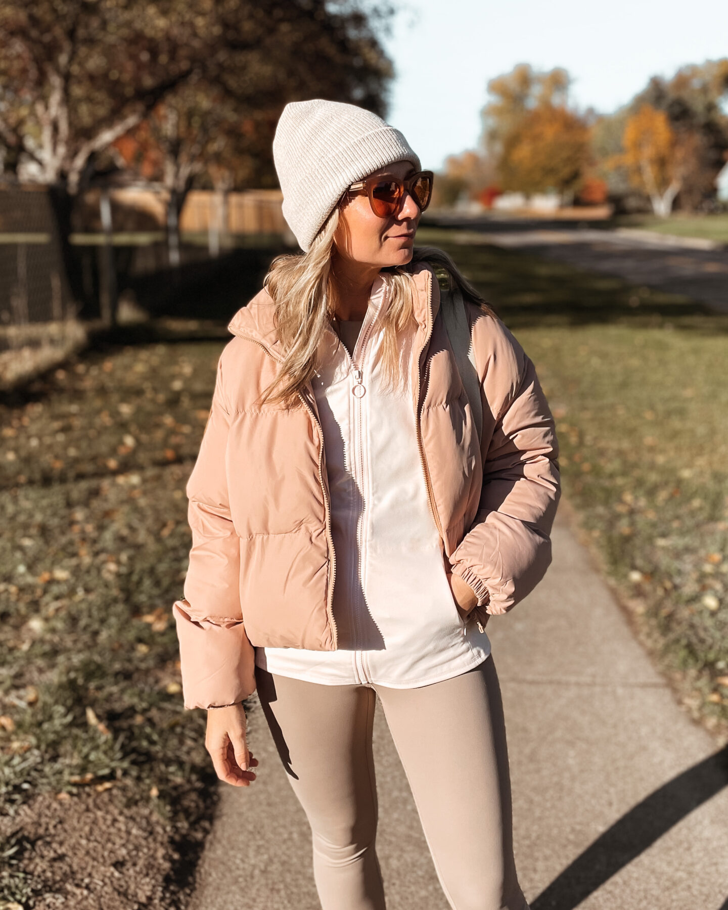 Karin Emily wears a fall sporty outfit with a pink track zip up, pink puffer coat, and taupe leggings