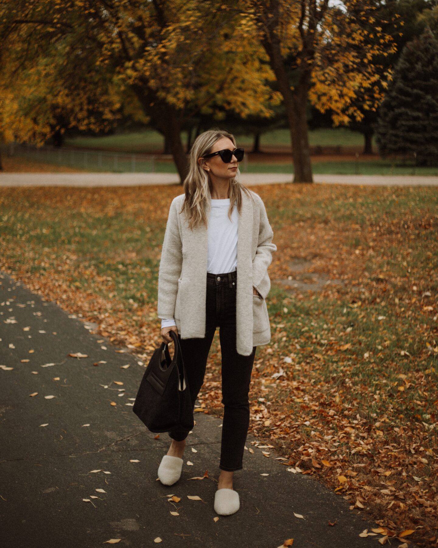 Karin Emily wears a Madewell shawl cardigan, white tee, black madewell perfect vintage jeans, a wool Hereu bag, and sherpa mules