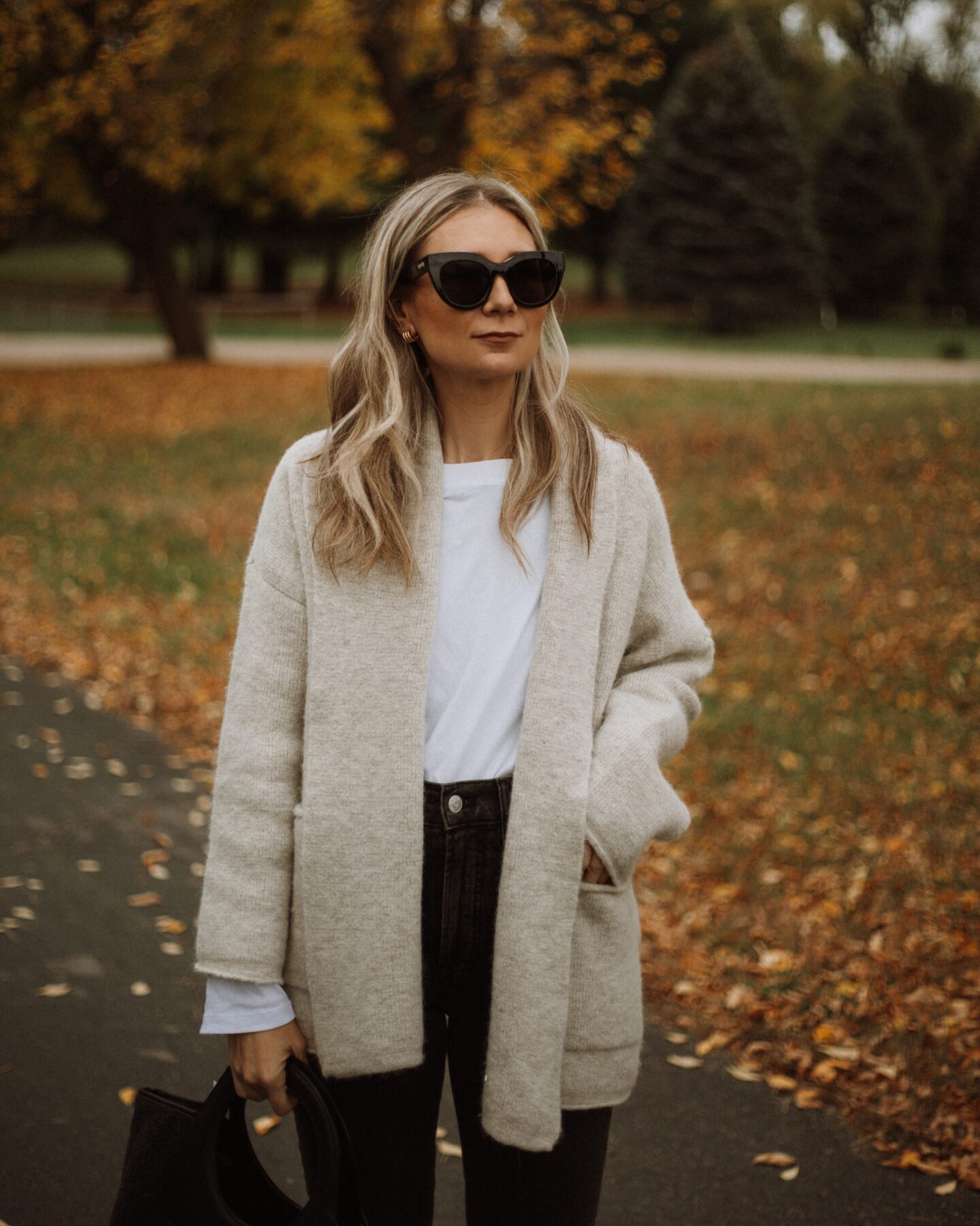 Karin Emily wears a Madewell shawl cardigan, white tee, black madewell perfect vintage jeans, and a wool Hereu bag,