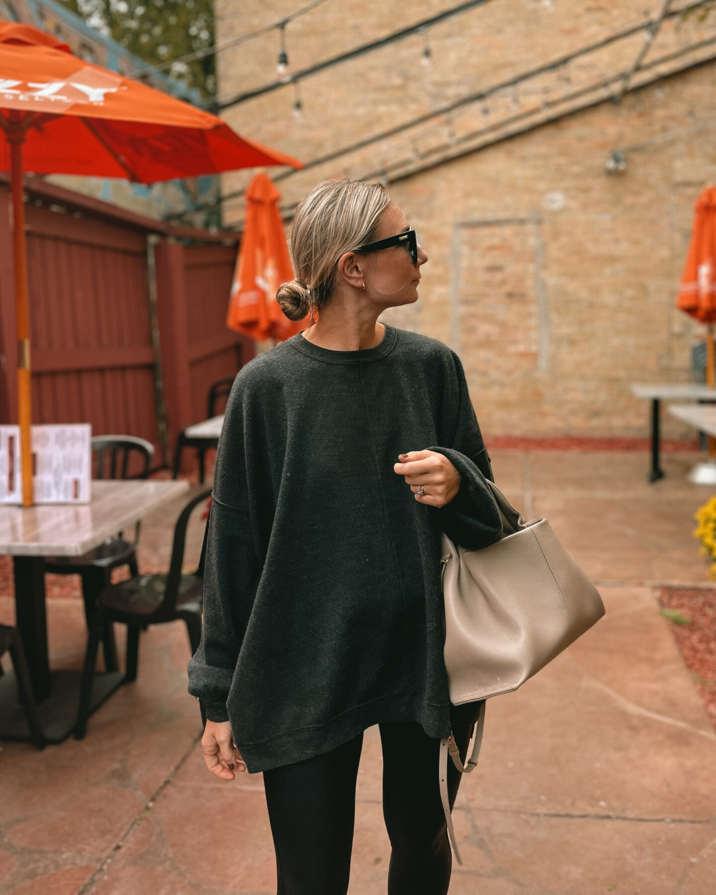 Karin Emily wears an oversized sweatshirt from free people over spanx faux leather leggings, and black and white new balance sneakers with a polene bag and black le specs air heart sunglasses 