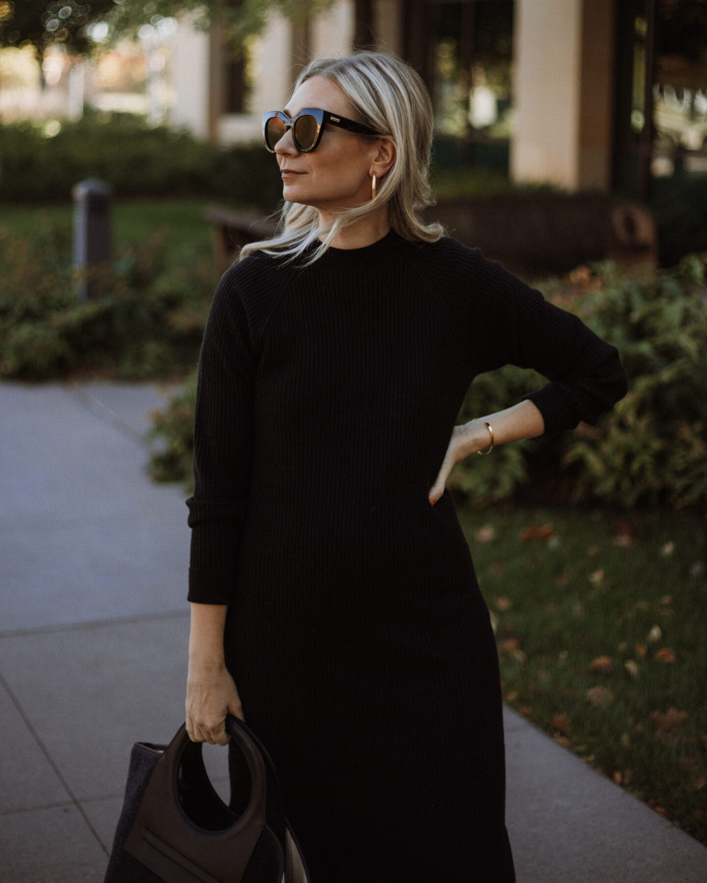 Karin Emily wears a black sweater dress, hereu bag, and oversized black sunglasses