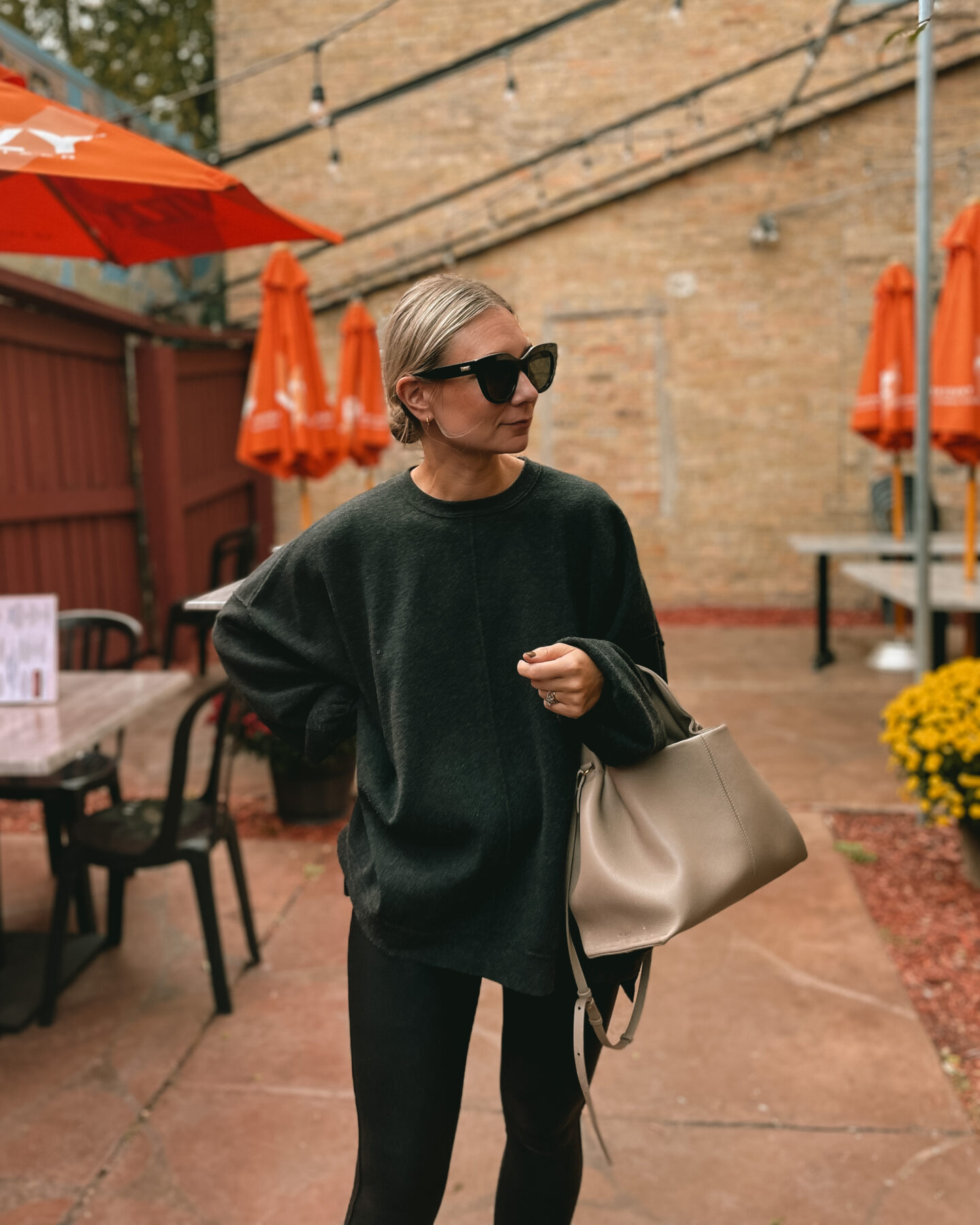 Karin Emily wears an oversized sweatshirt from free people over spanx faux leather leggings, and black and white new balance sneakers with a polene bag and black le specs air heart sunglasses 