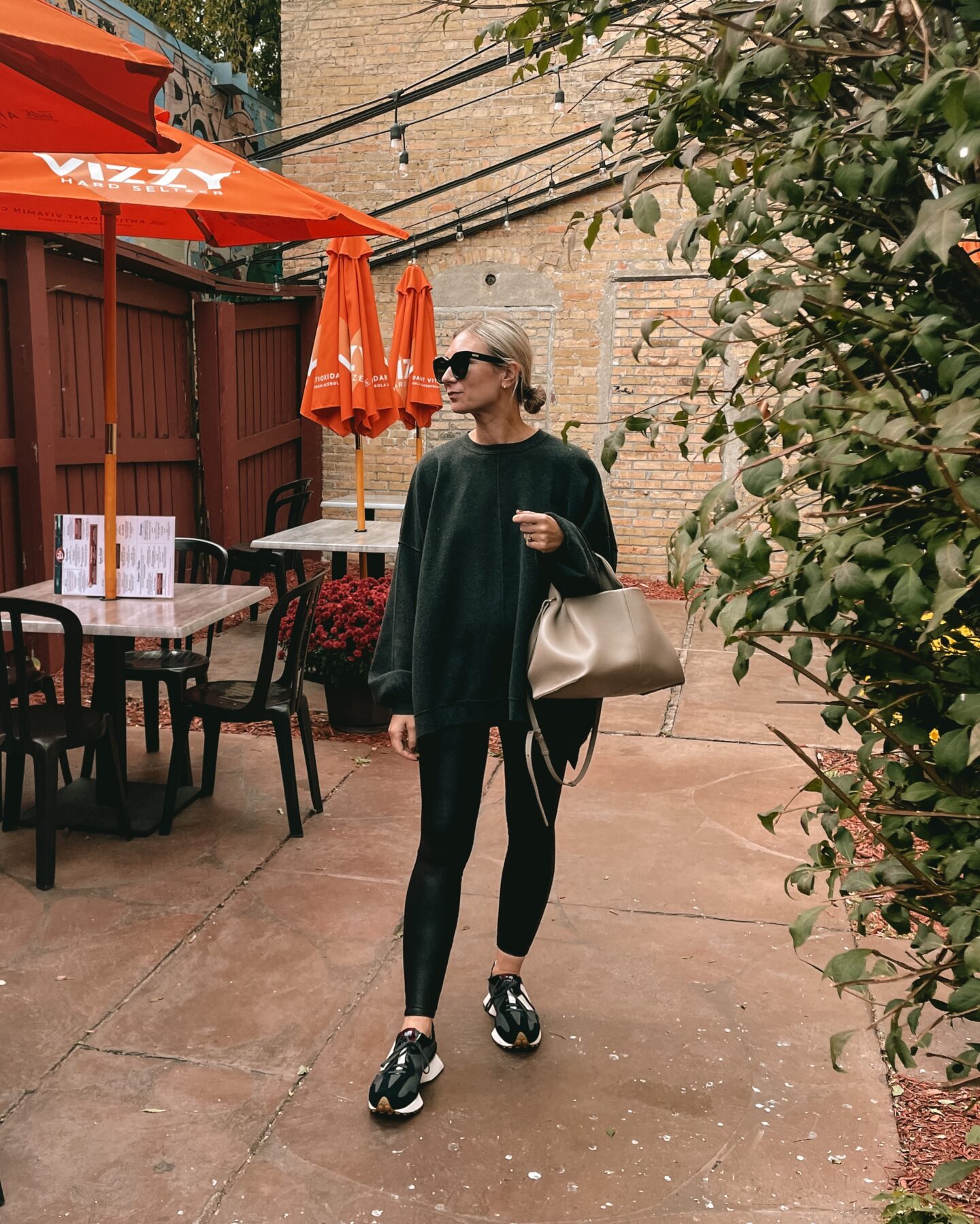 Karin Emily wears an oversized sweatshirt from free people over spanx faux leather leggings, and black and white new balance sneakers with a polene bag and black le specs air heart sunglasses