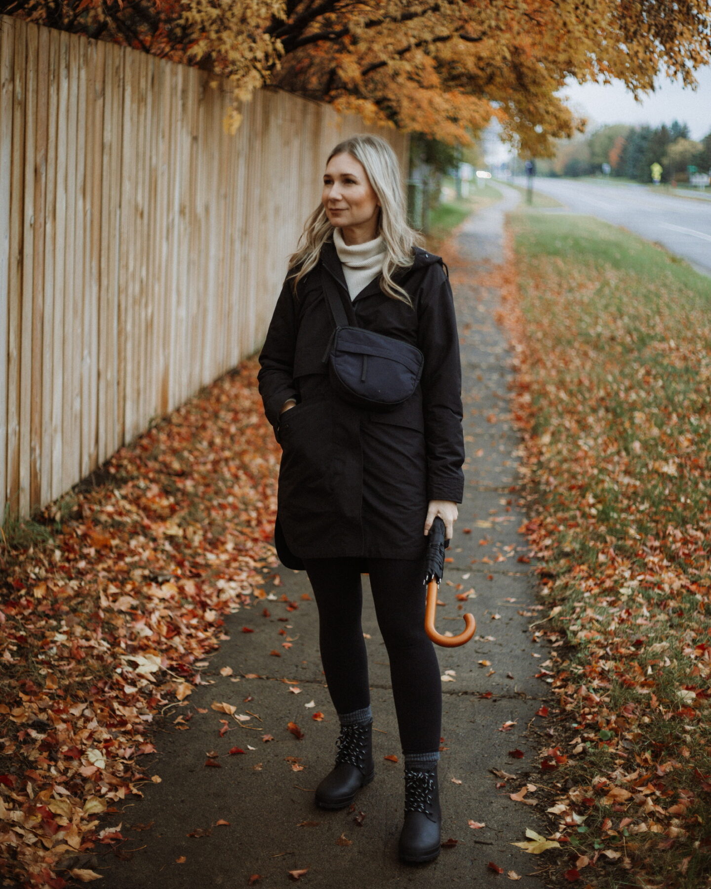 Karin Emily wears a black rain coat, black leggings, and black rain boots