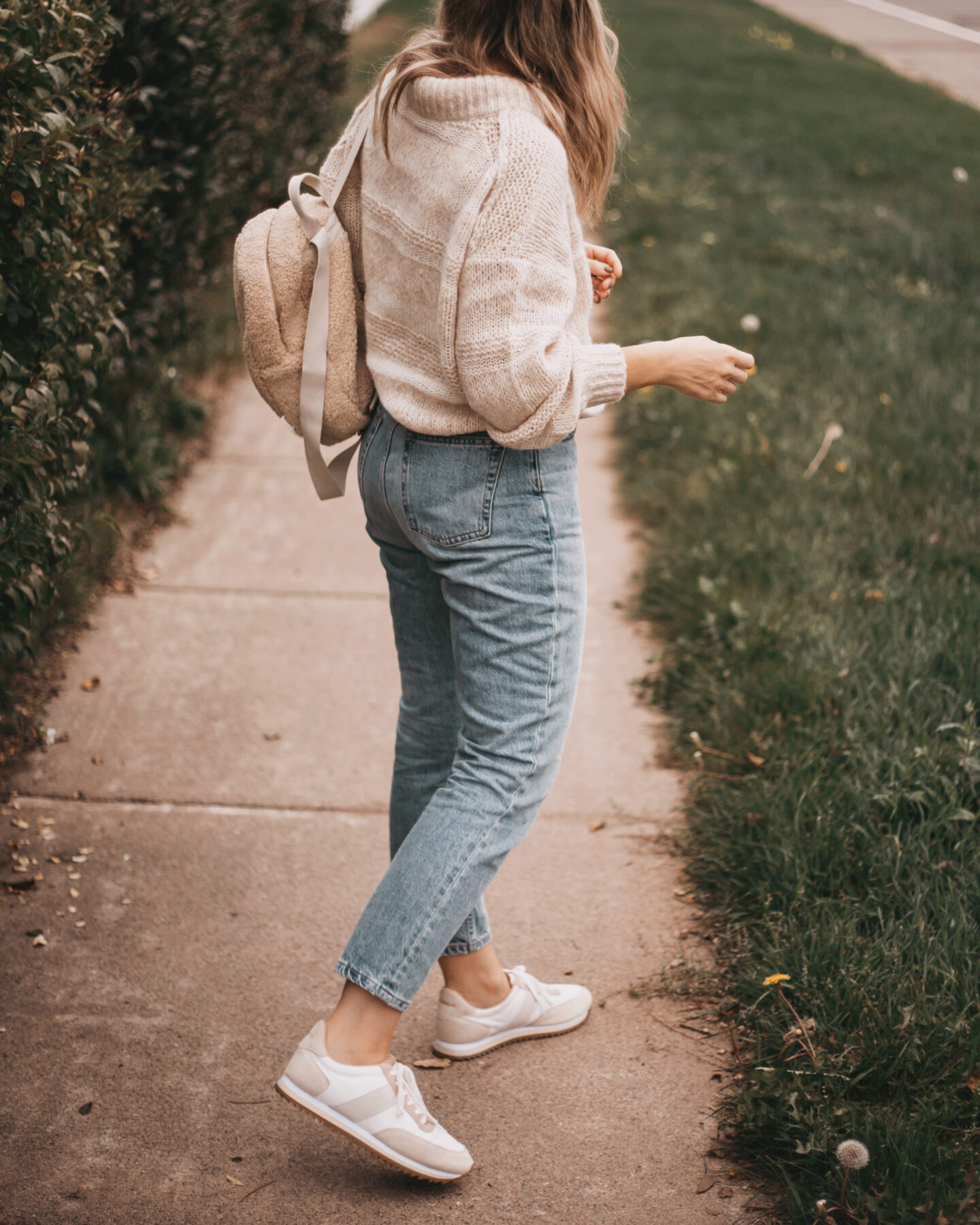 karin emily wears a chunky sweater, light wash jeans, and neutral sneakers