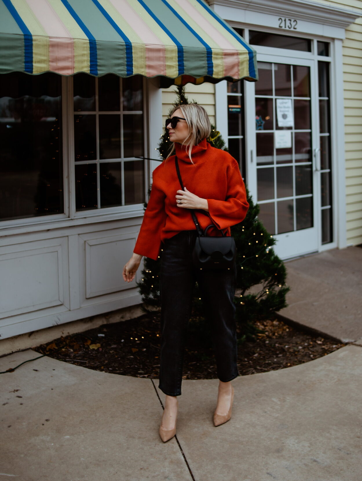 Karin Emily wears a red cashmere sweater, black jeans, nude sude heels, and a polene numero un nano