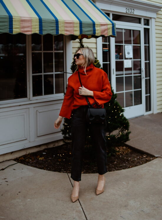 Karin Emily wears a red cashmere sweater, black jeans, nude sude heels, and a polene numero un nano