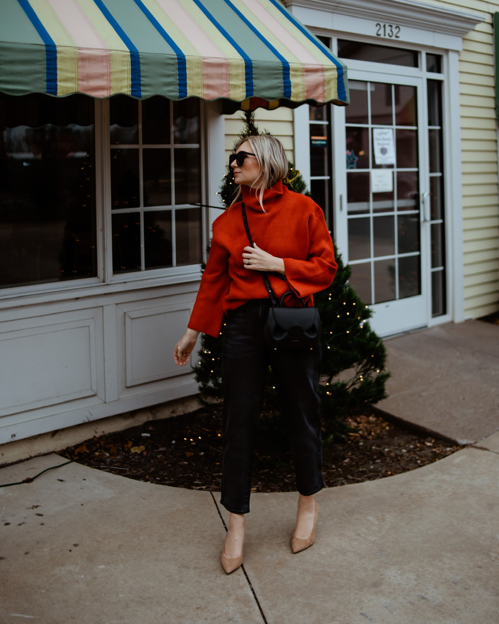 Karin Emily wears a red cashmere sweater, black jeans, nude sude heels, and a polene numero un nano