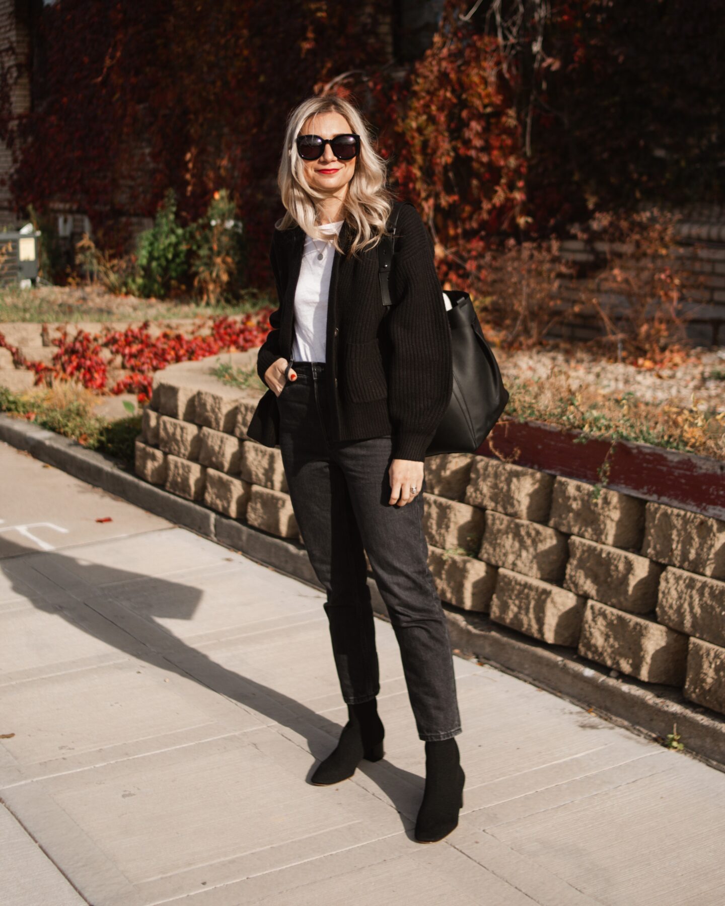 Karin Emily wears a casual holiday outfit with a black cardigan, white tee, black jeans, black boots, and a black bag all with new pieces from Everlane