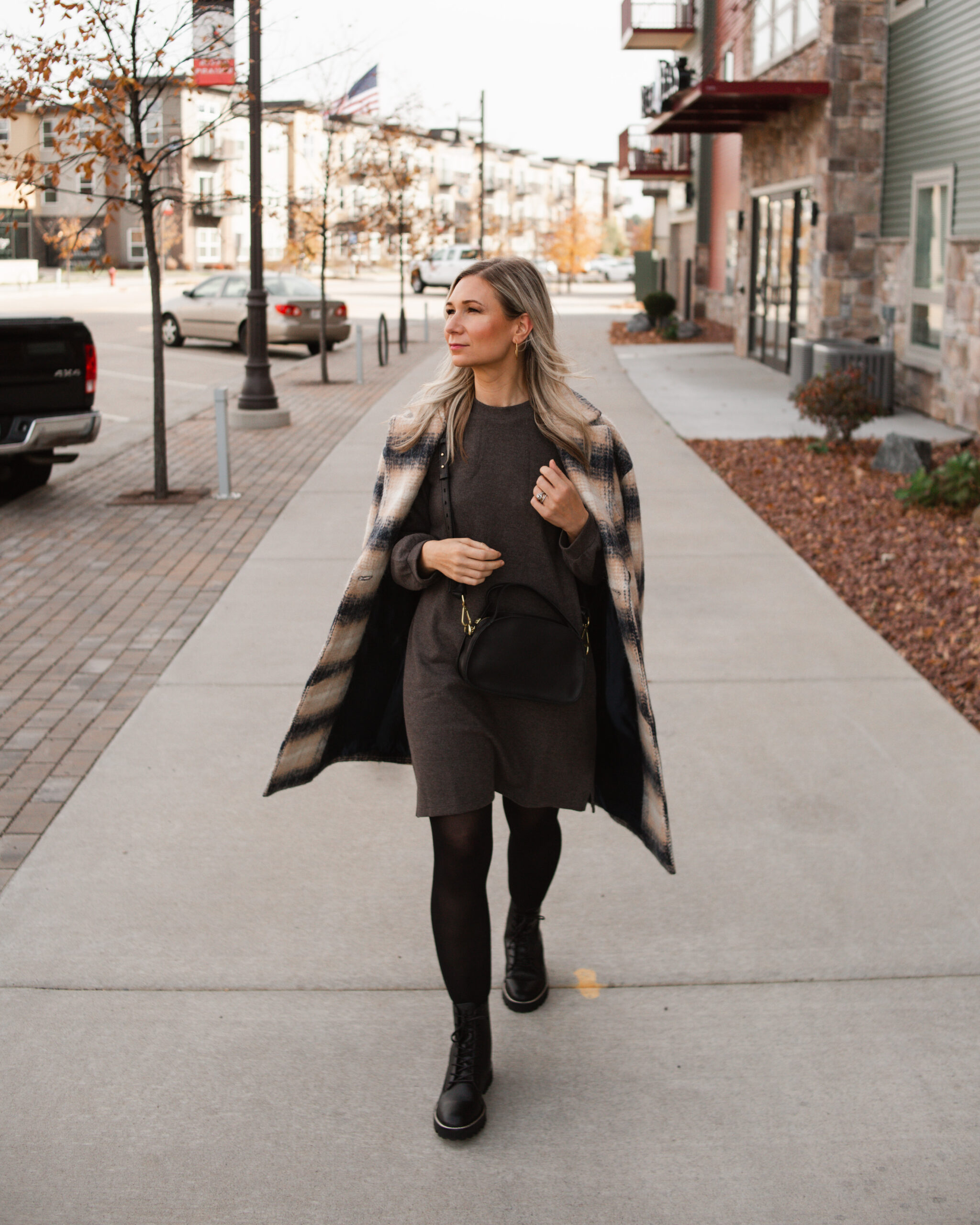 Karin Emily wears a plaid coat and charcoal sweater dress and black combat boots from Madewell