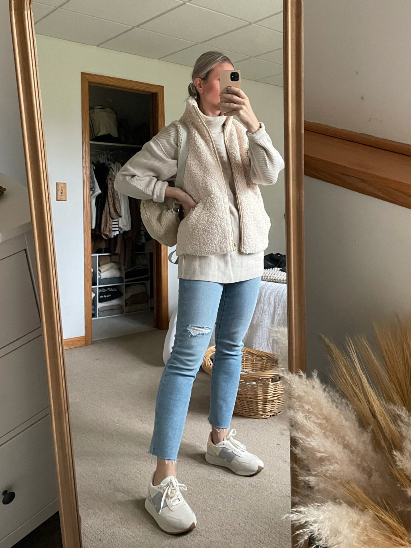 Karin Emily wears a Free People Tunic Sweater, Sherpa Vest, Light Wash Jeans, and New Balance Sneakers