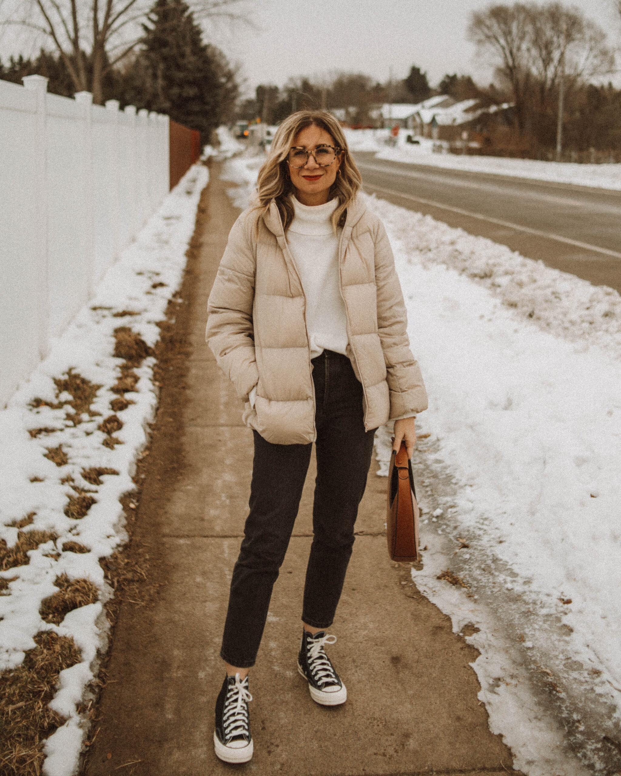 Karin Emily wears a white turtleneck sweater, cream puffer coat, washed black jeans, and black high top converse