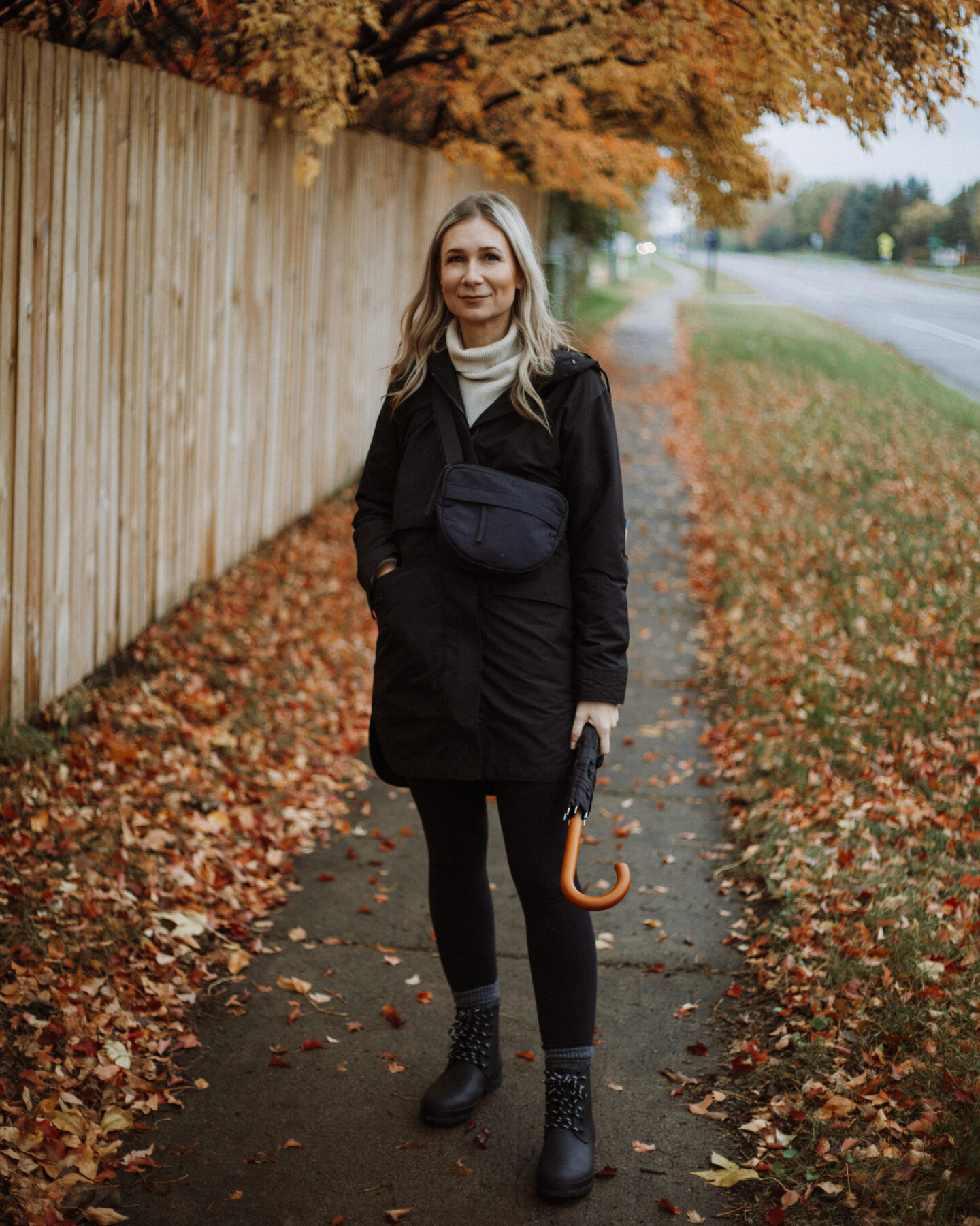 Karin Emily wears a black rain coat, black leggings, and black rain boots