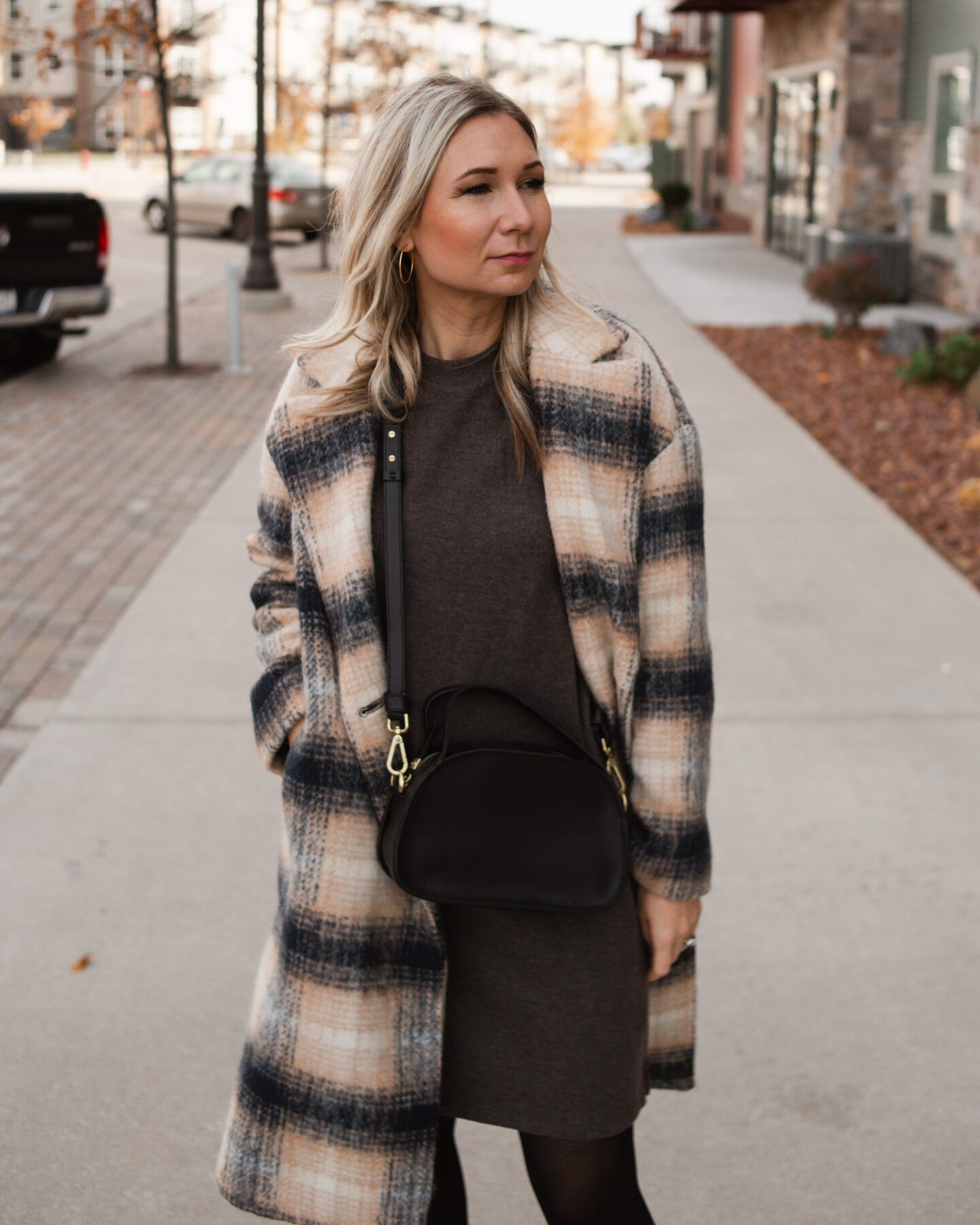 Karin Emily wears a plaid coat and charcoal sweater dress from Madewell