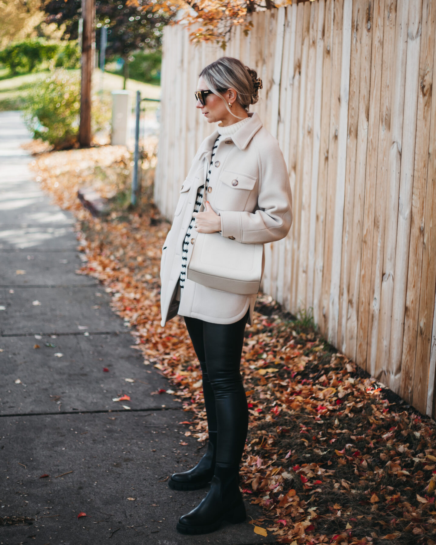 Karin Emily wears a black and white striped sweater from ABLE, black faux leather leggings, black lug boots from Sam Edelman, and a shirt jacket from Sezane