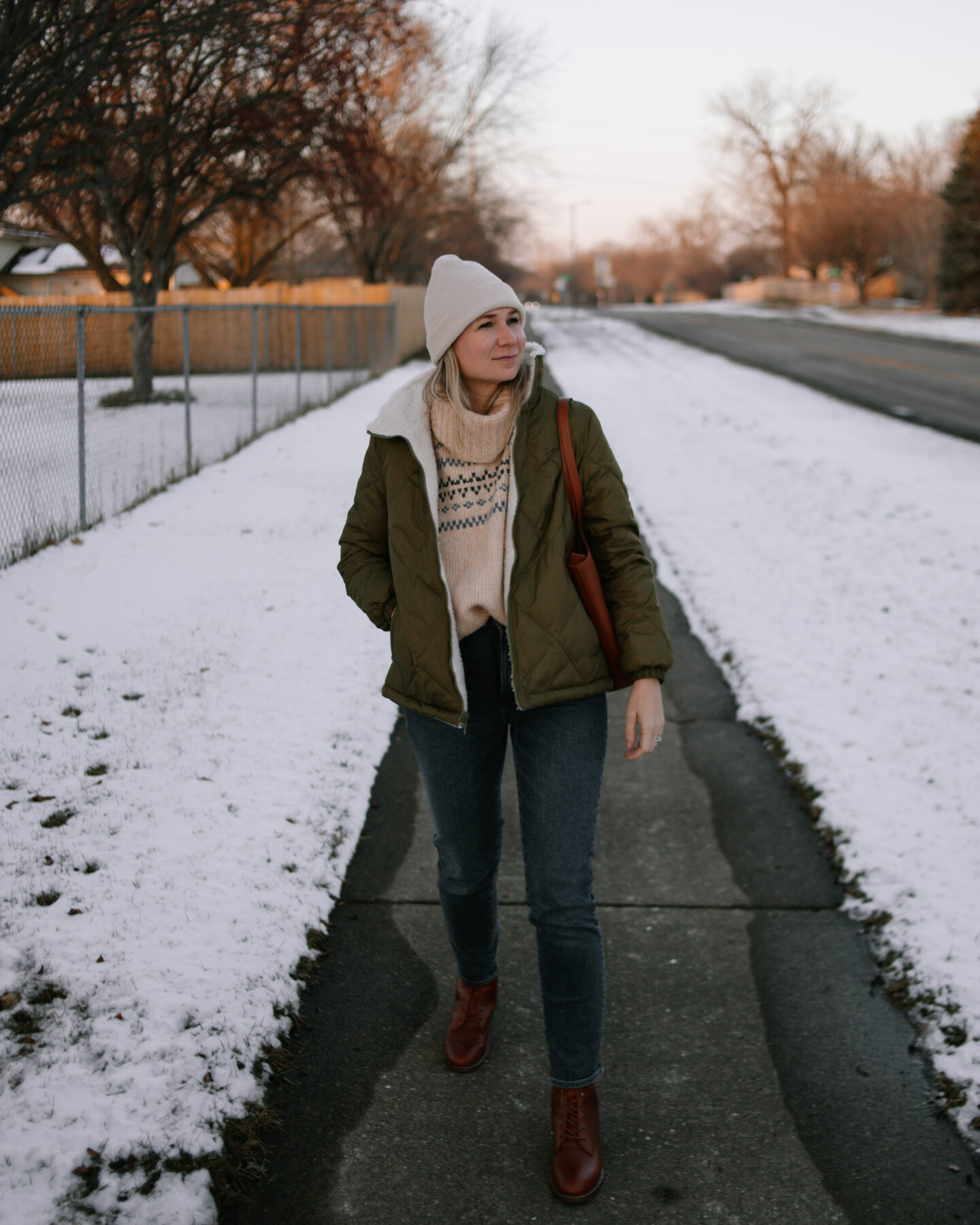 Karin Emily wears an olive green puffer coat, dark wash straight leg jeans, a brown tote bag, and brown lace up boots