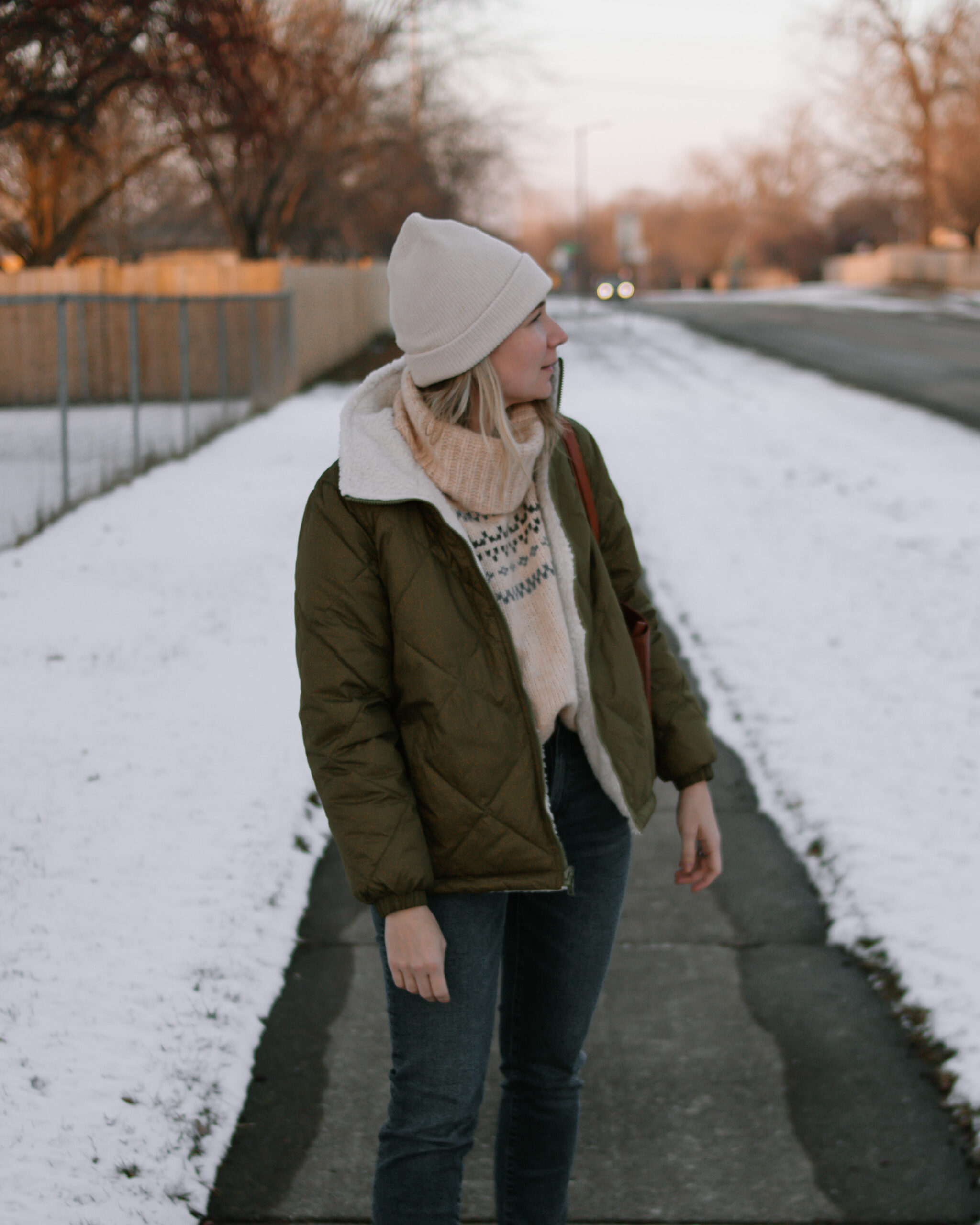 Karin Emily wears an olive green puffer coat, dark wash straight leg jeans, a brown tote bag, and brown lace up boots