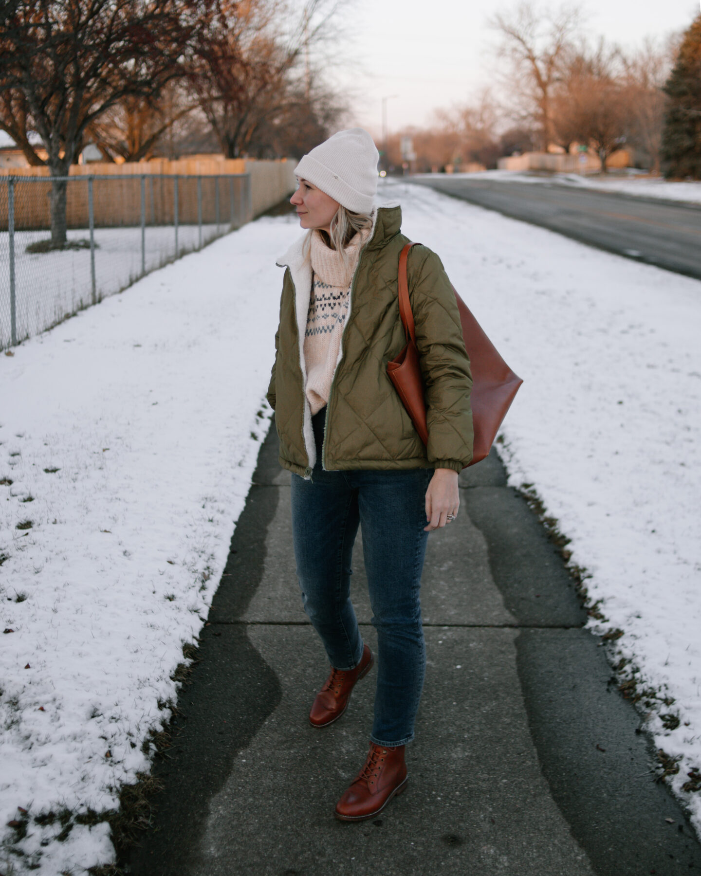 Karin Emily wears an olive green puffer coat, dark wash straight leg jeans, a brown tote bag, and brown lace up boots