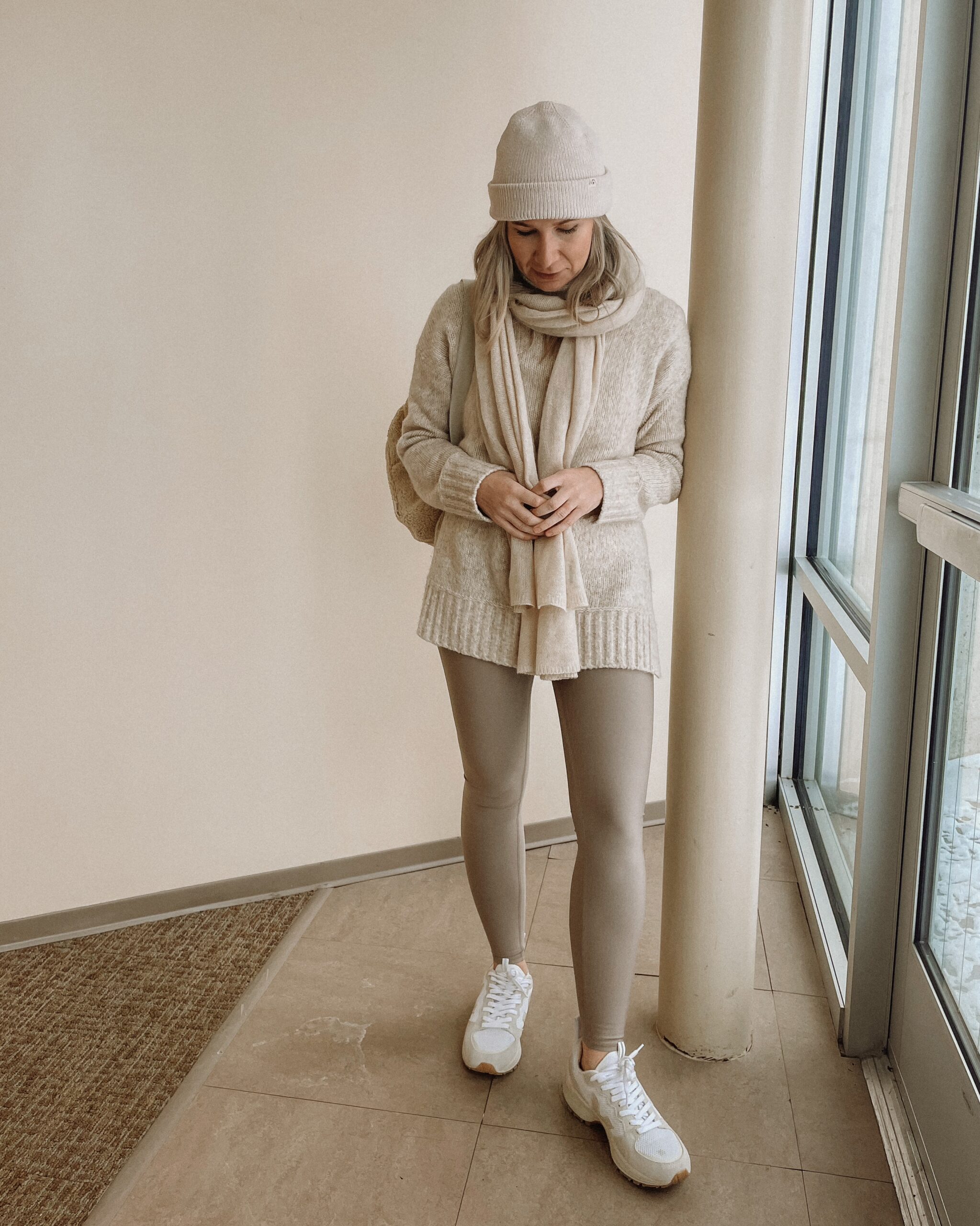 Karin Emily Wears a pair of taupe leggings from Alo Yoga with an oatmeal tunic sweater and Veja Venturi sneakers