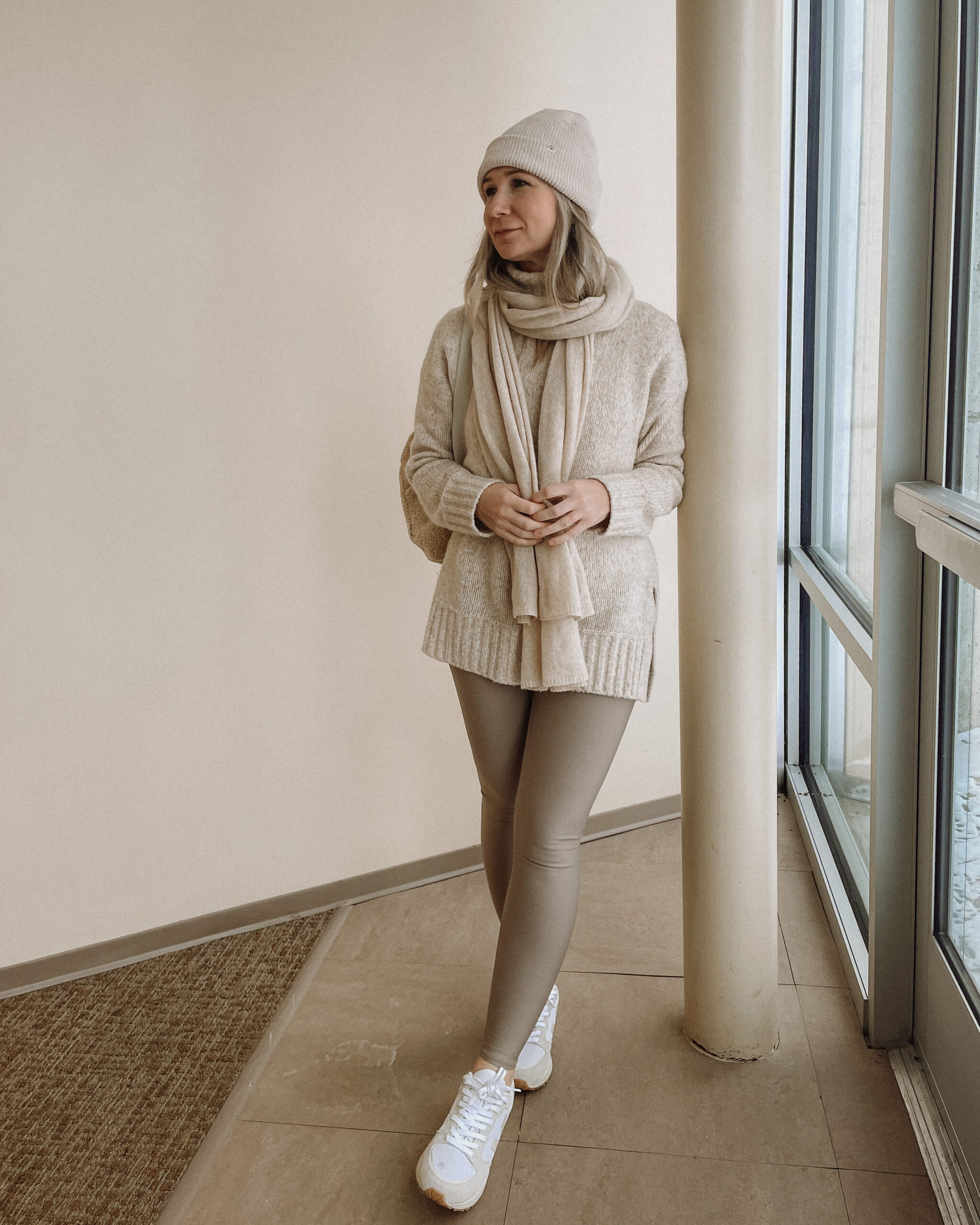 Karin Emily Wears a pair of taupe leggings from Alo Yoga with an oatmeal tunic sweater and Veja Venturi sneakers