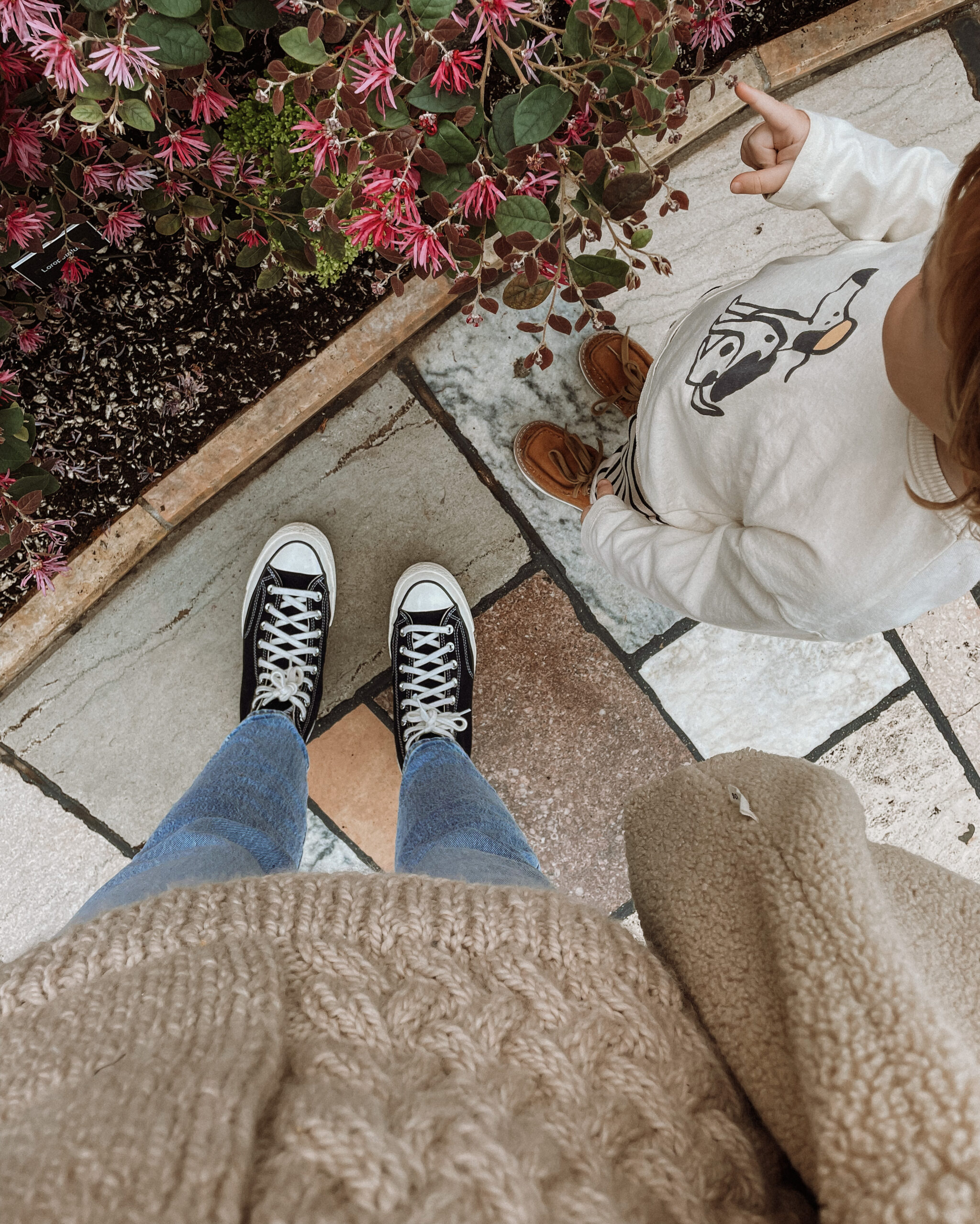 Karin Emily wears a pair of lightwash Levi's Jeans, a cableknit tunic length sweater and black high top Converse