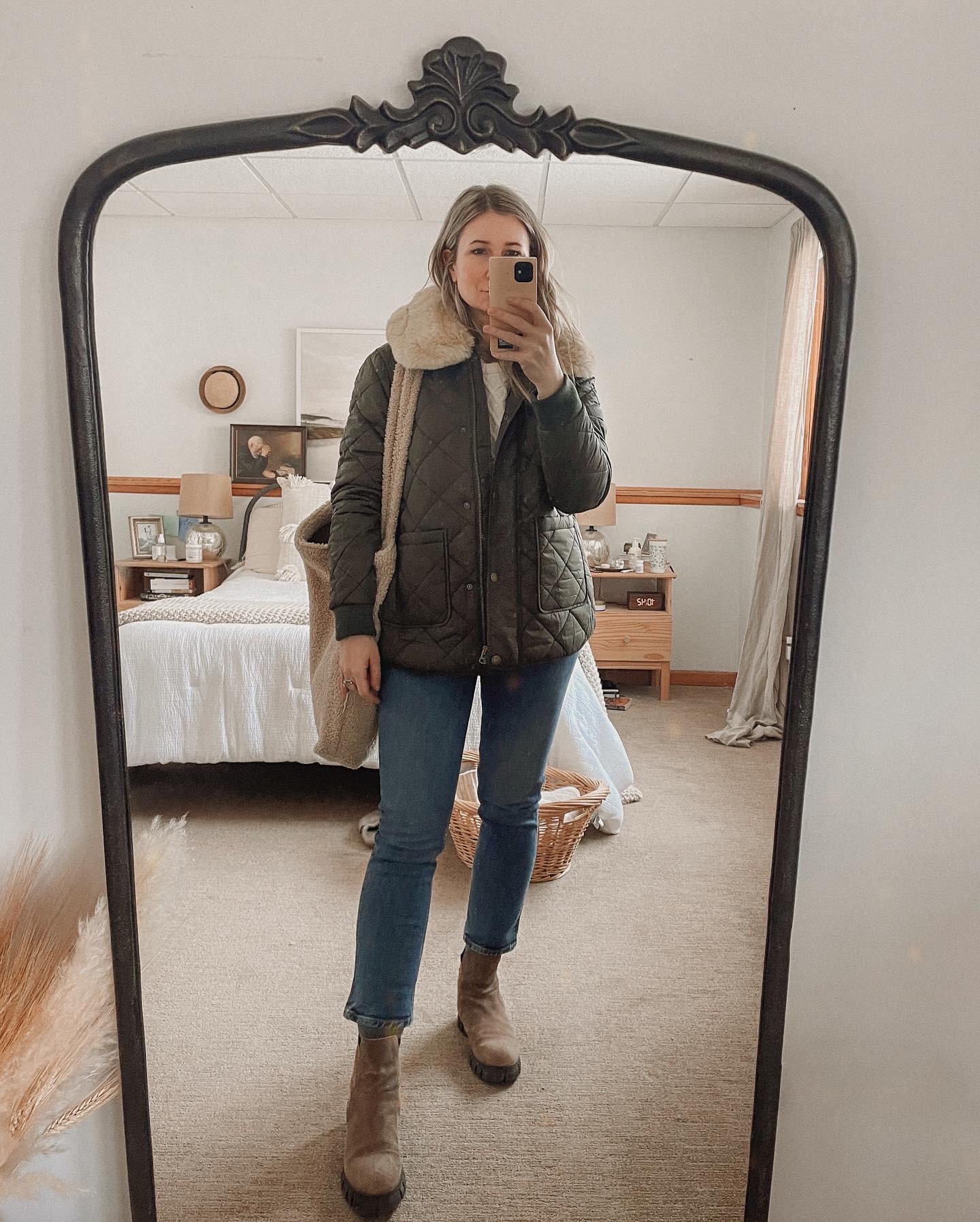 Karin Emily wears an olive green puffer coat with faux fur collar, mid wash blue jeans, and brown lug boots