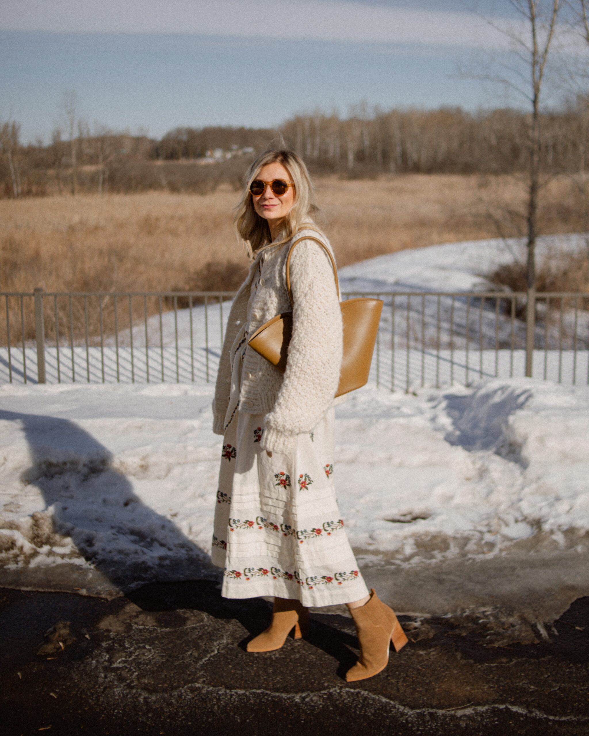 Karin Emily wears a floral spring dress with a chunky knit over her shoulders and a little liffner tulip bag