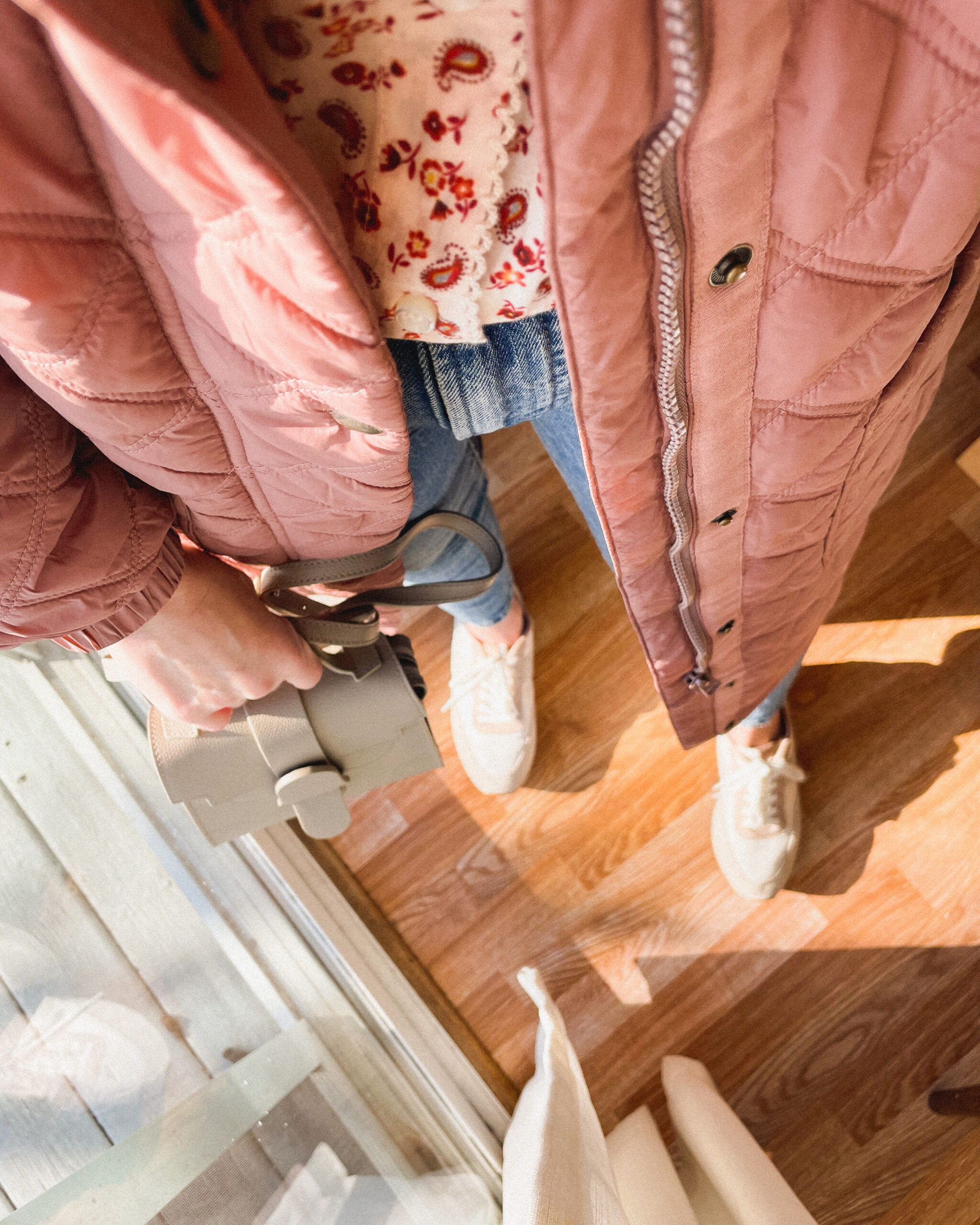 Karin Emily wears a pink quilted coat, pink floral top from Doen, Madewell perfect vintage jeans, and pink sneakers
