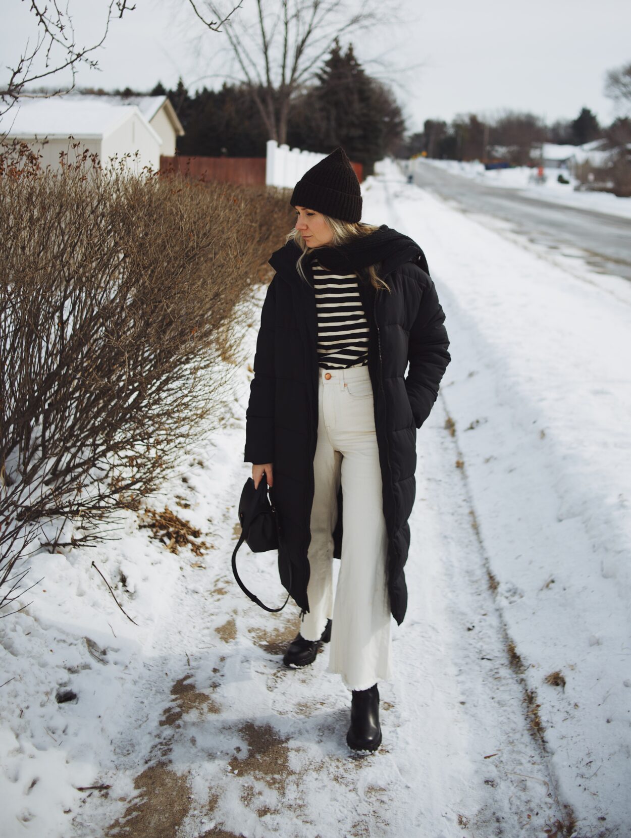 Karin Emily wears a breton stripe tee, long black puffer coat, white wide leg jeans, black lug boots, and a black polene bag