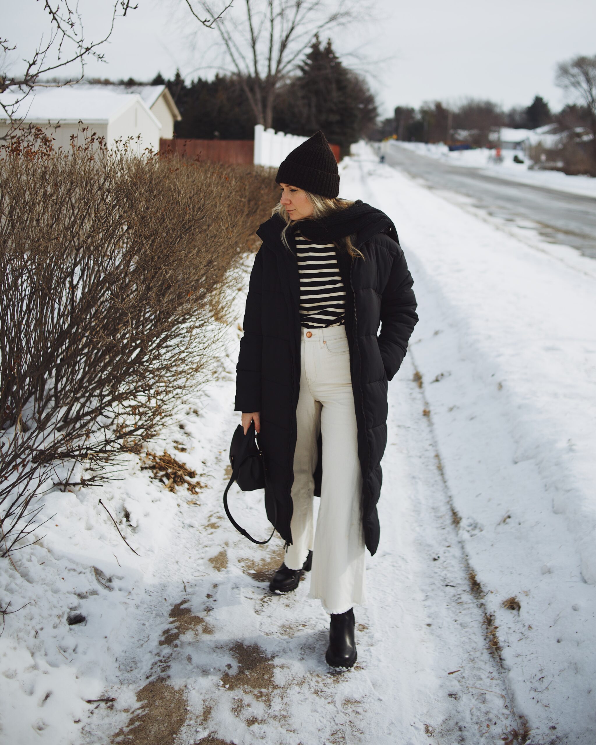 Karin Emily wears a breton stripe tee, long black puffer coat, white wide leg jeans, black lug boots, and a black polene bag