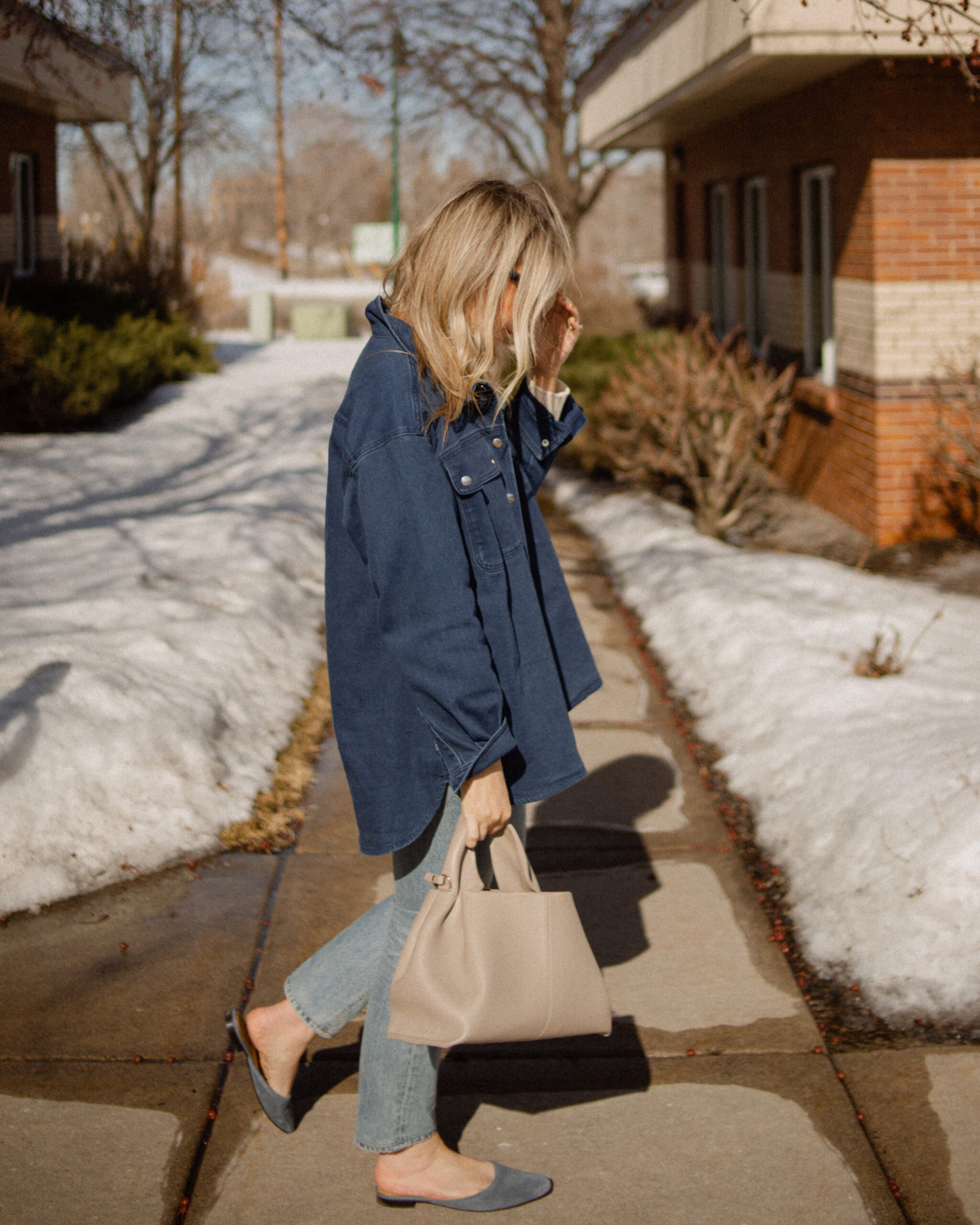 Karin Emily wears a Breton stripe sweater under a denim shirt jacket paired with a pair of light wash jeans and a blue suede pair of mules