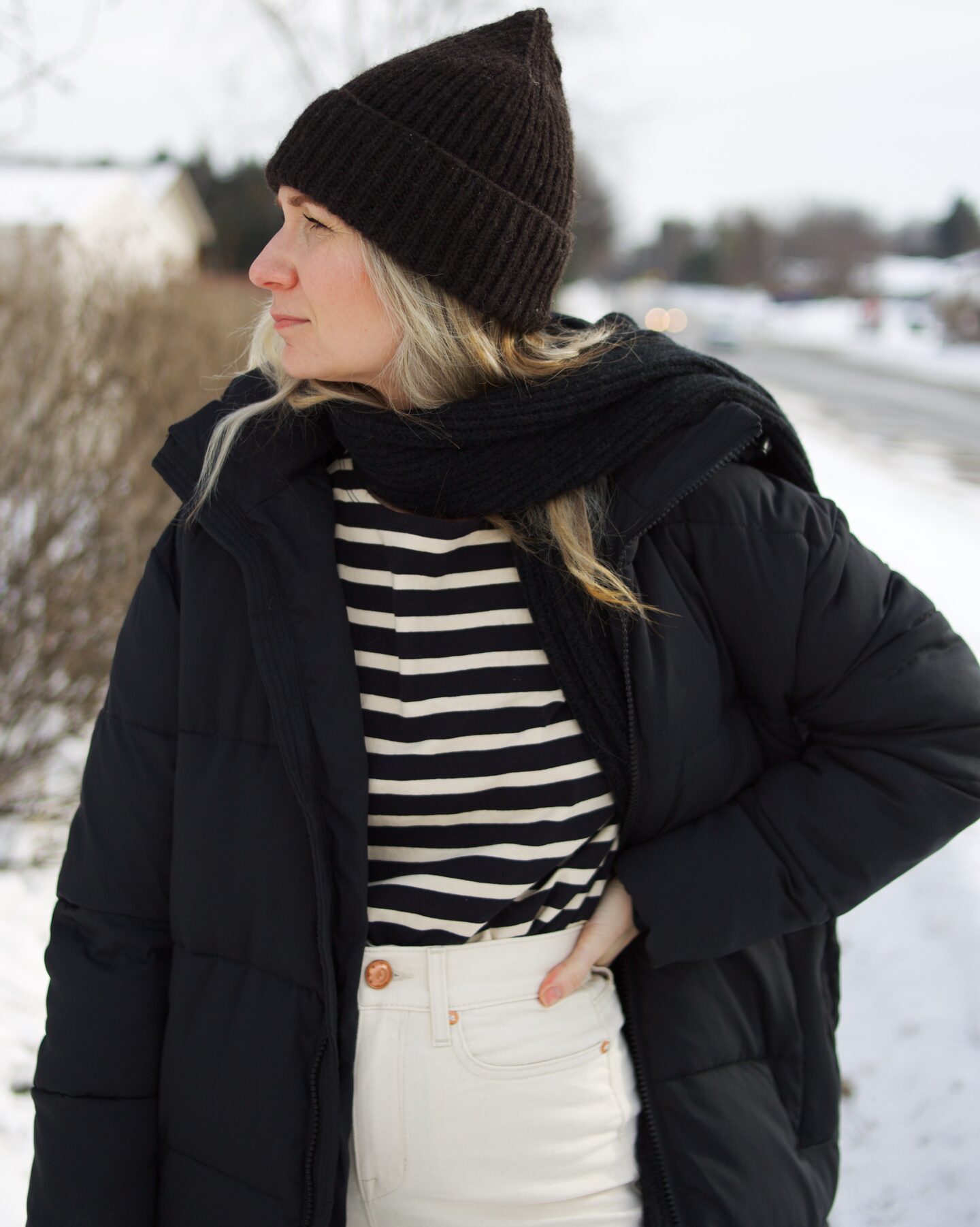 Karin Emily wears a breton stripe tee, long black puffer coat, and white wide leg jeans